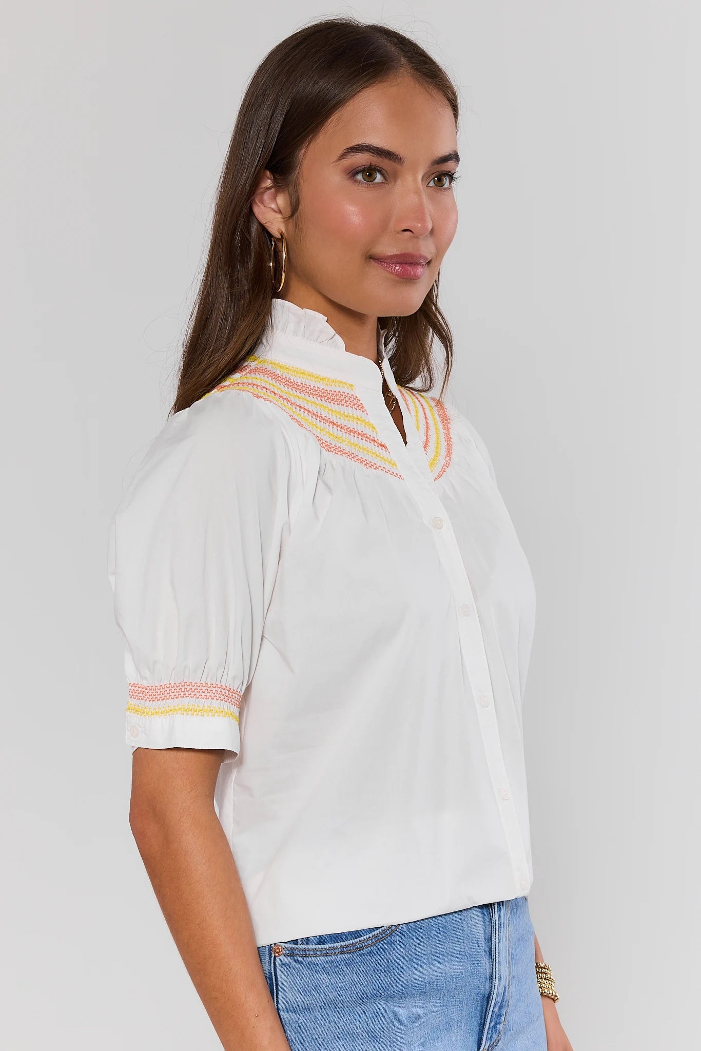 side shot Woman wearing a white blouse with colorful accents on a plain background