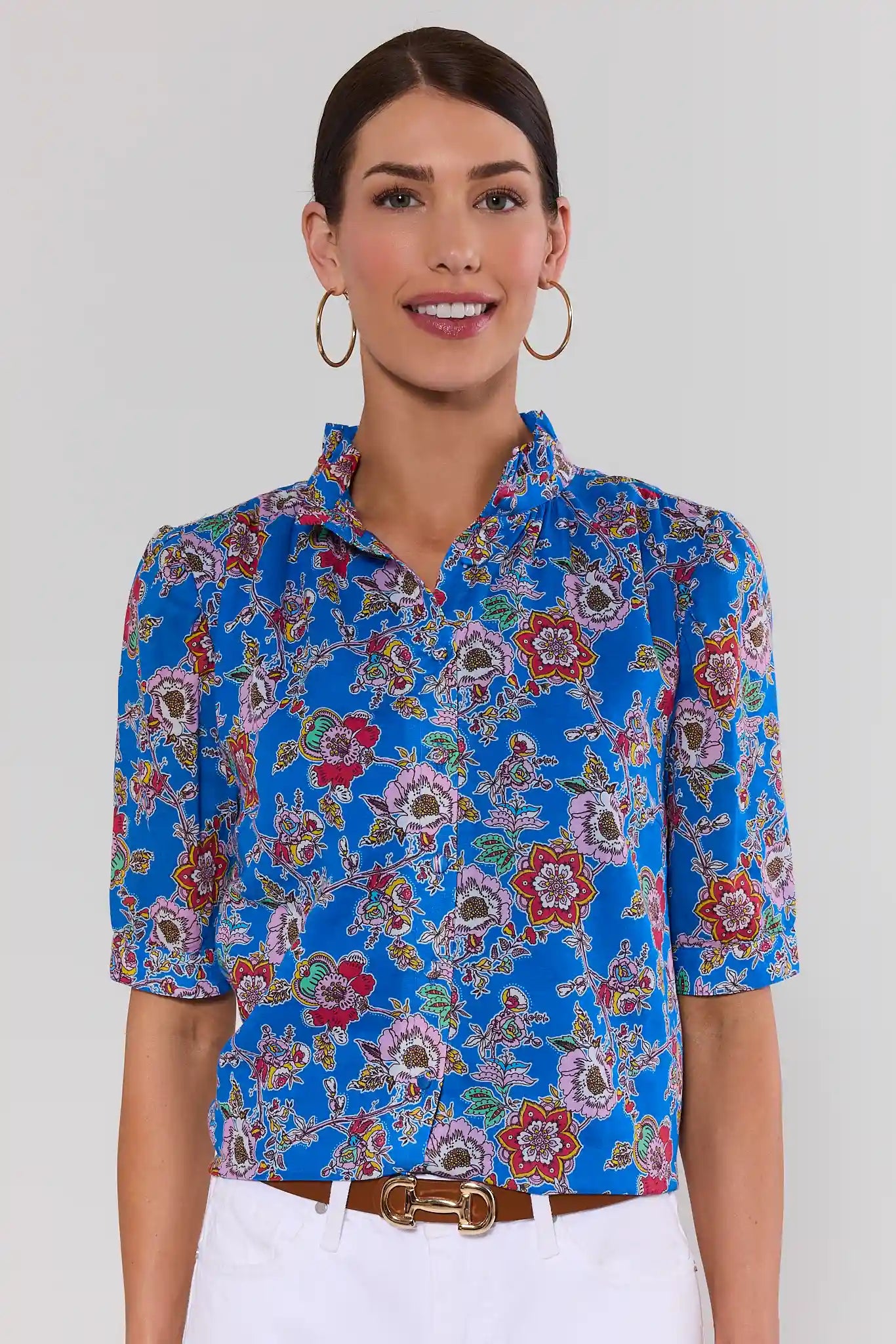 Woman standing wearing a blue floral blouse against a plain background
