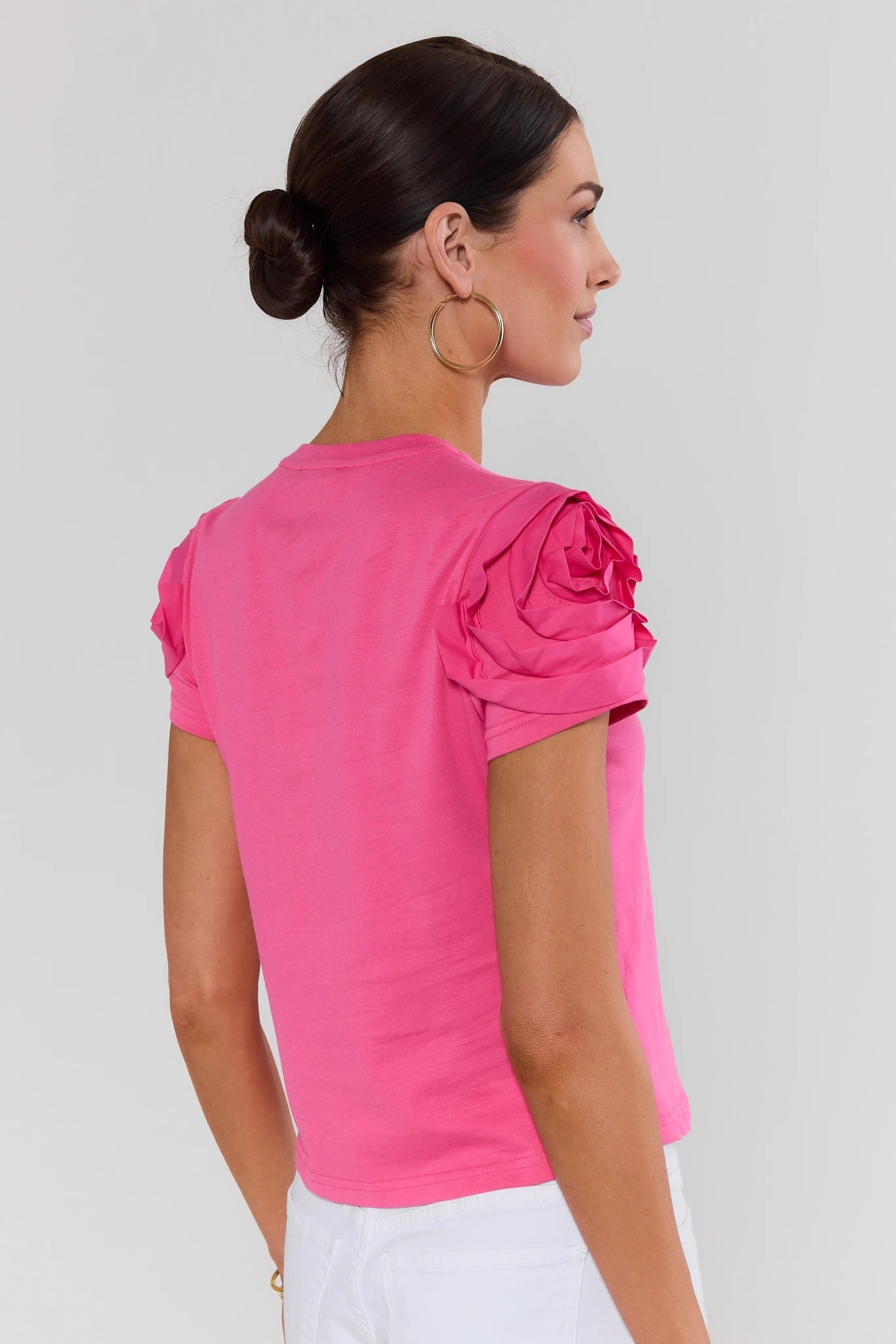 Woman standing wearing a pink blouse with ruffled sleeves on a plain background
