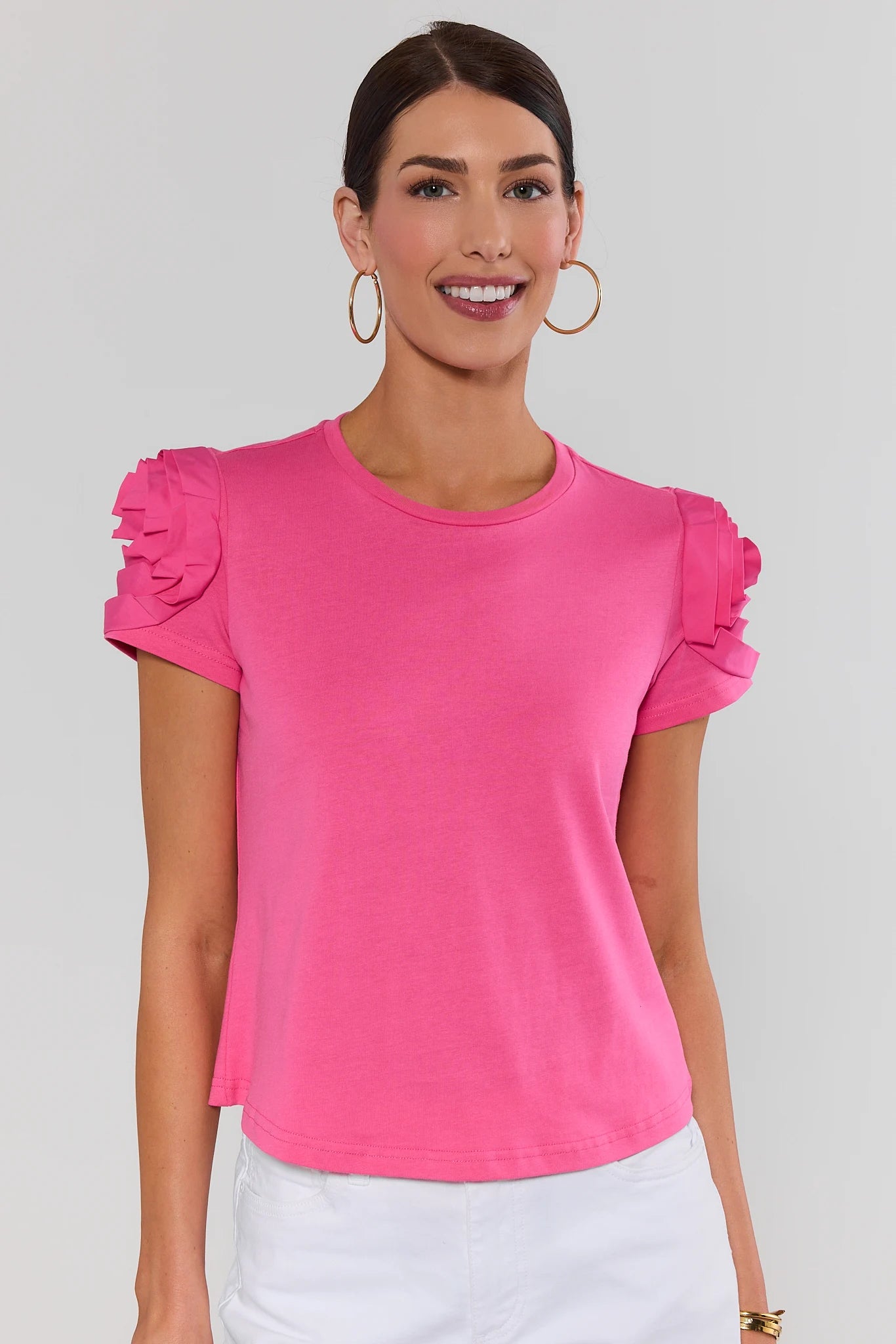 Woman wearing a bright pink top with ruffled sleeves on a plain background