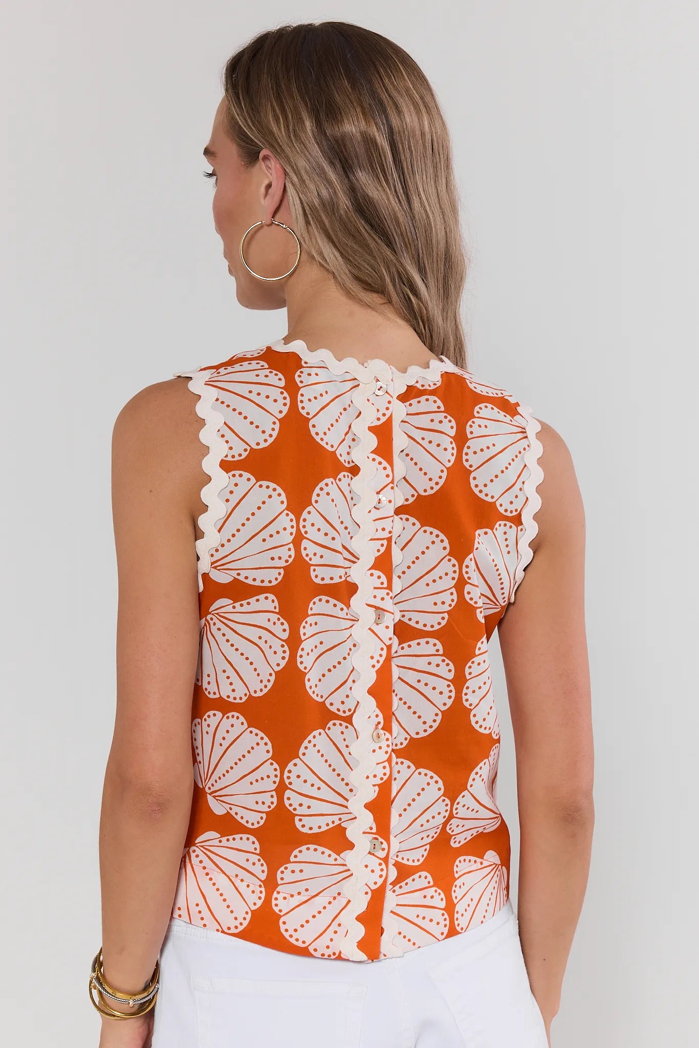 Woman wearing a sleeveless top with white shell pattern on an orange background standing