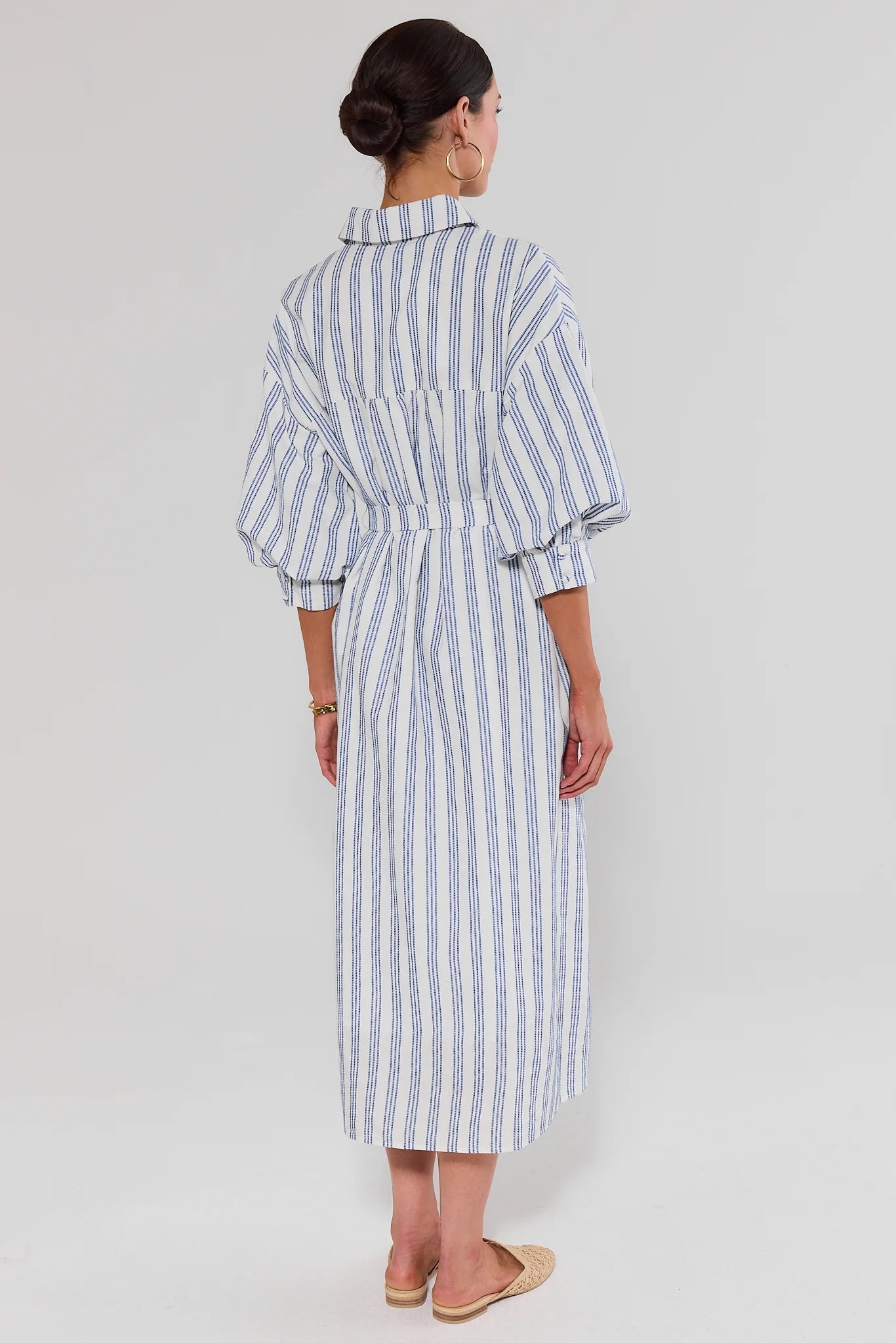 Woman wearing a blue and white striped dress on a plain background standing