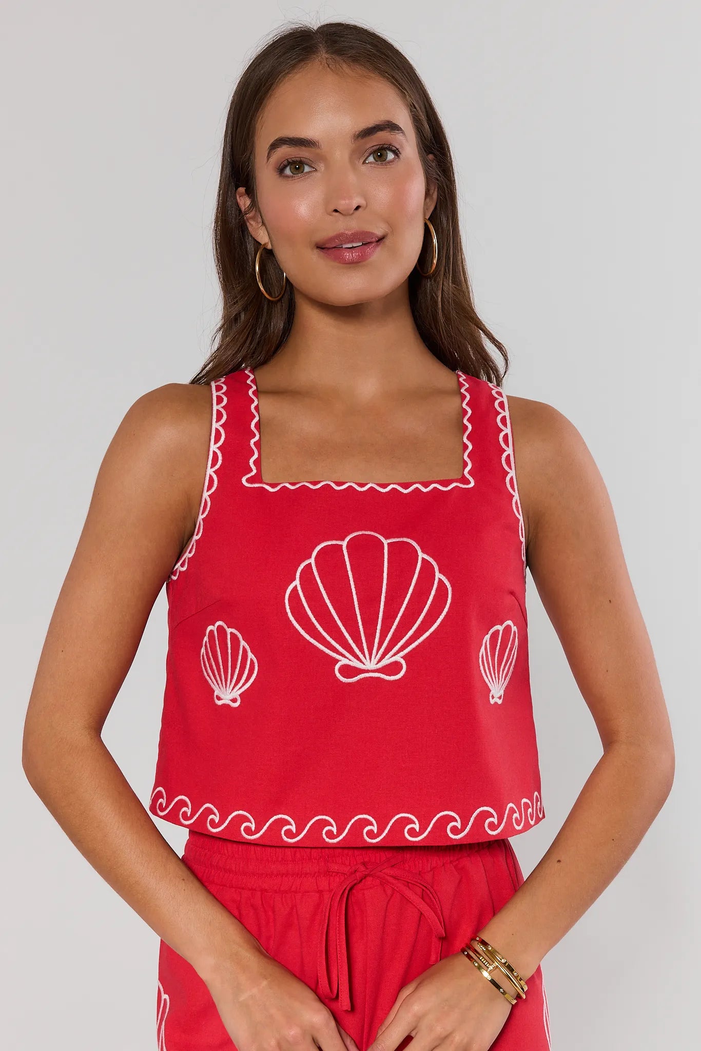 Woman wearing a red sleeveless top with shell designs on a plain background