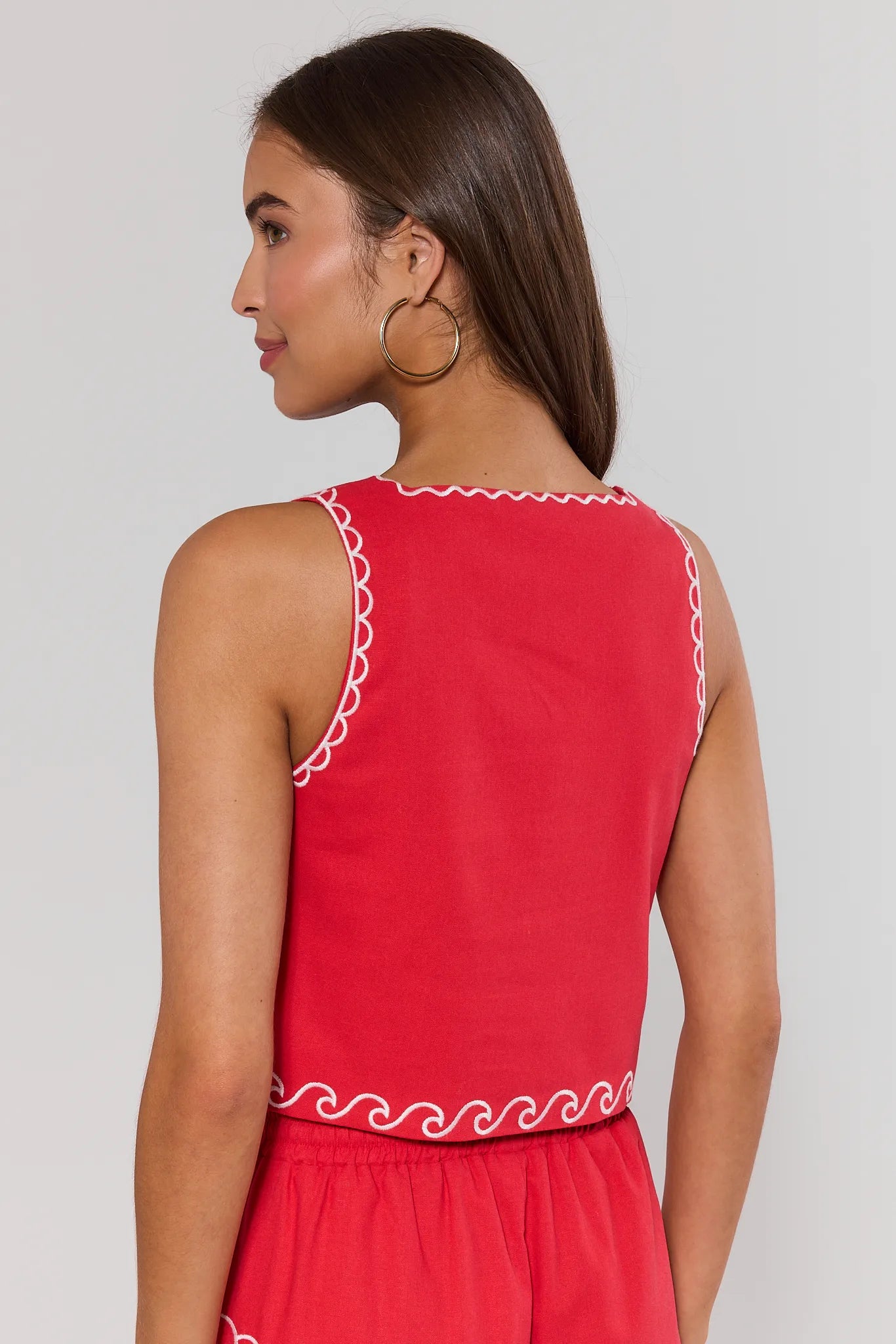 Woman standing wearing a red seashell top with white trim on a plain background