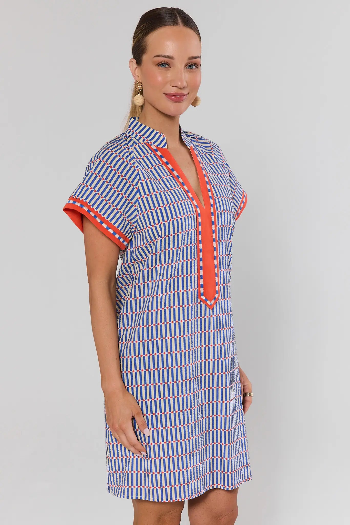 side shot Woman wearing a blue and white patterned dress with orange accents on a gray background