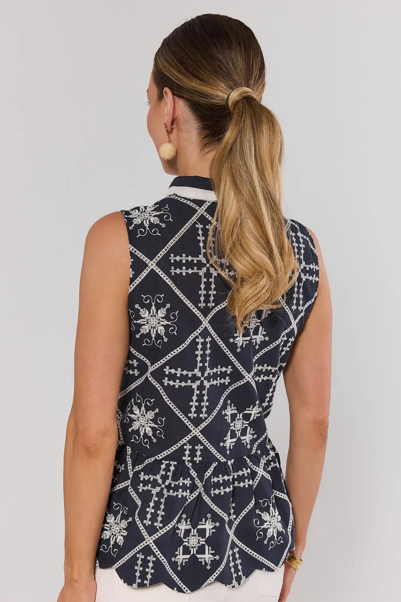 Woman wearing a sleeveless black and white patterned top against a plain background standing