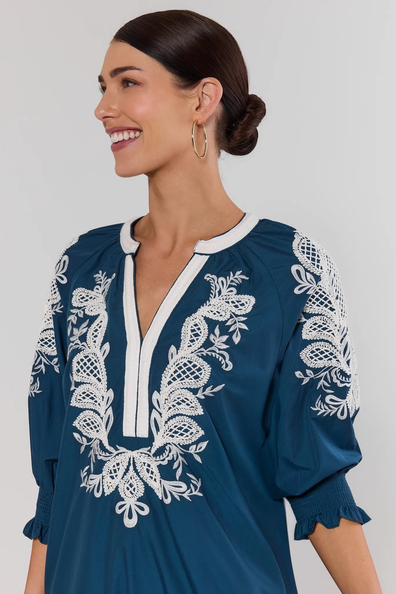 Woman wearing a blue dress with white embroidery on a plain background close up