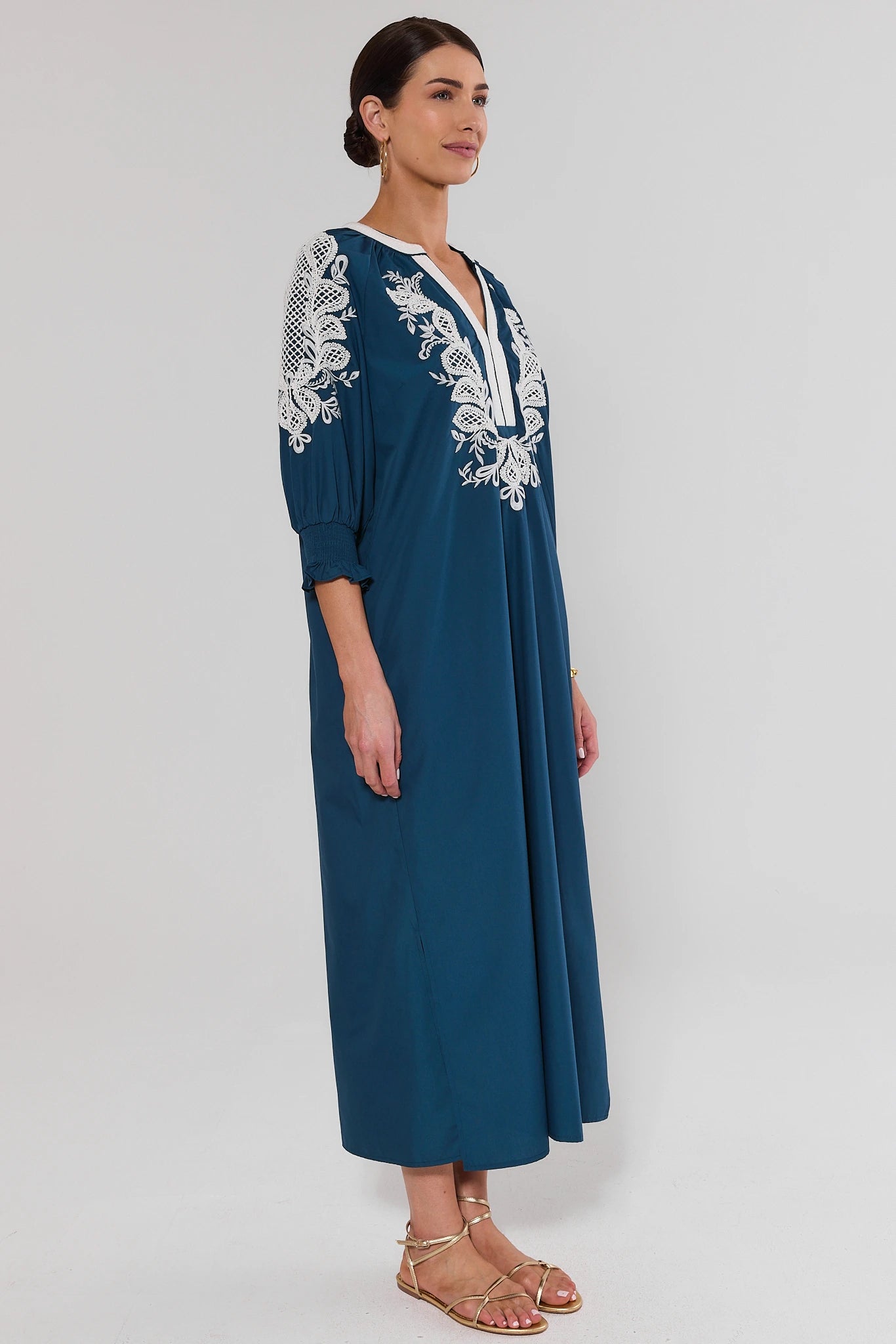 side shot Woman wearing a blue dress with white embroidery on a white background