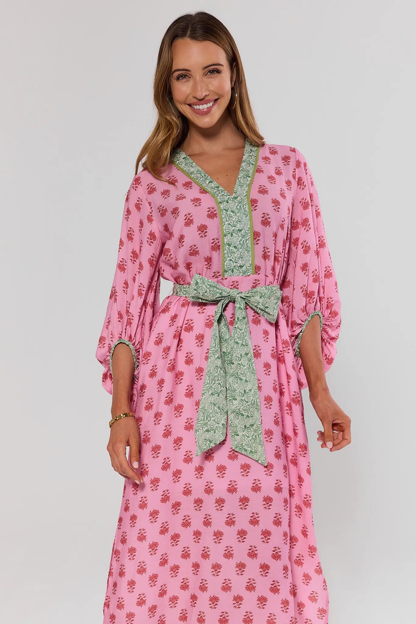 Woman wearing a pink floral dress with a green belt against a white background