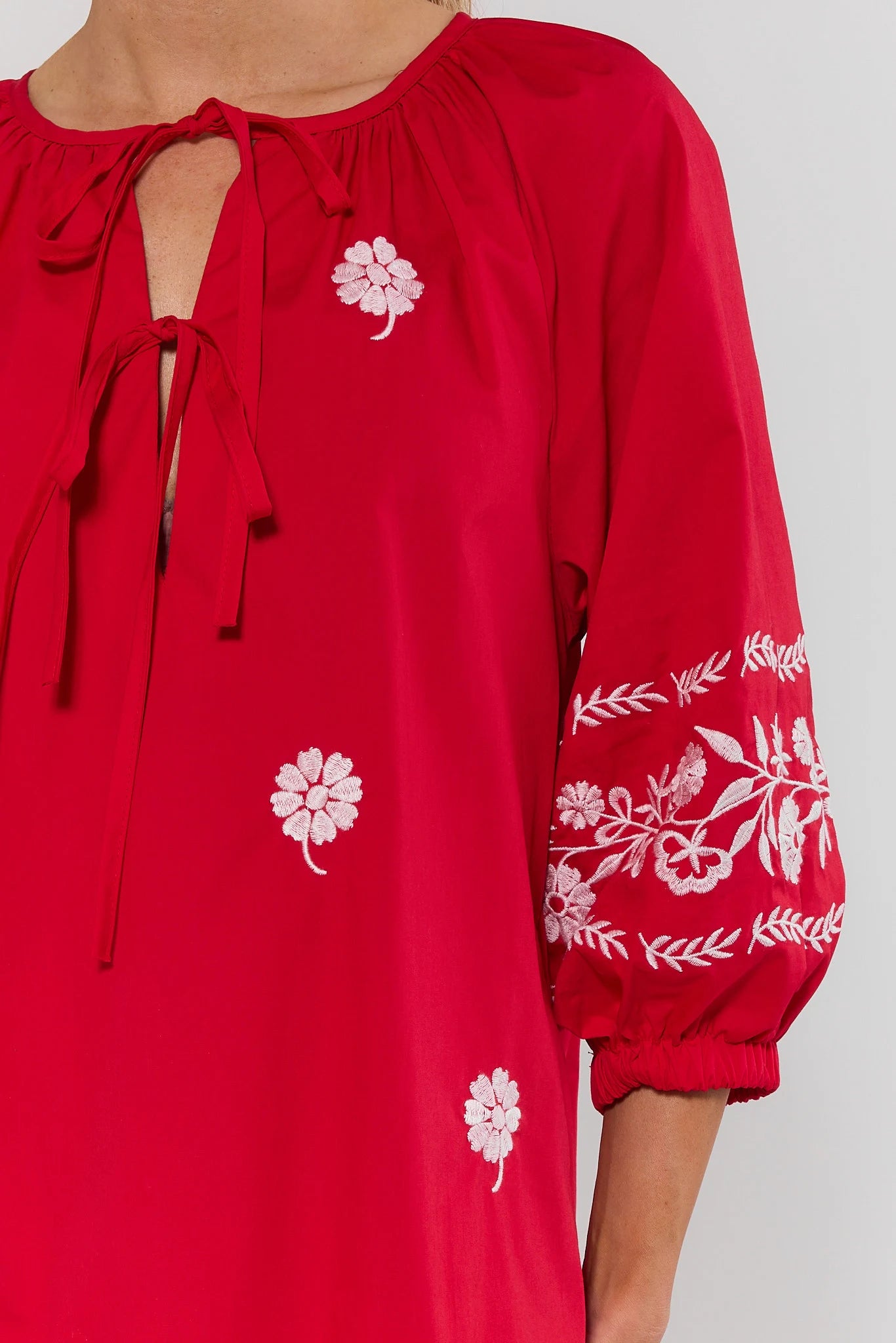 close up Red dress with white floral embroidery on a plain background