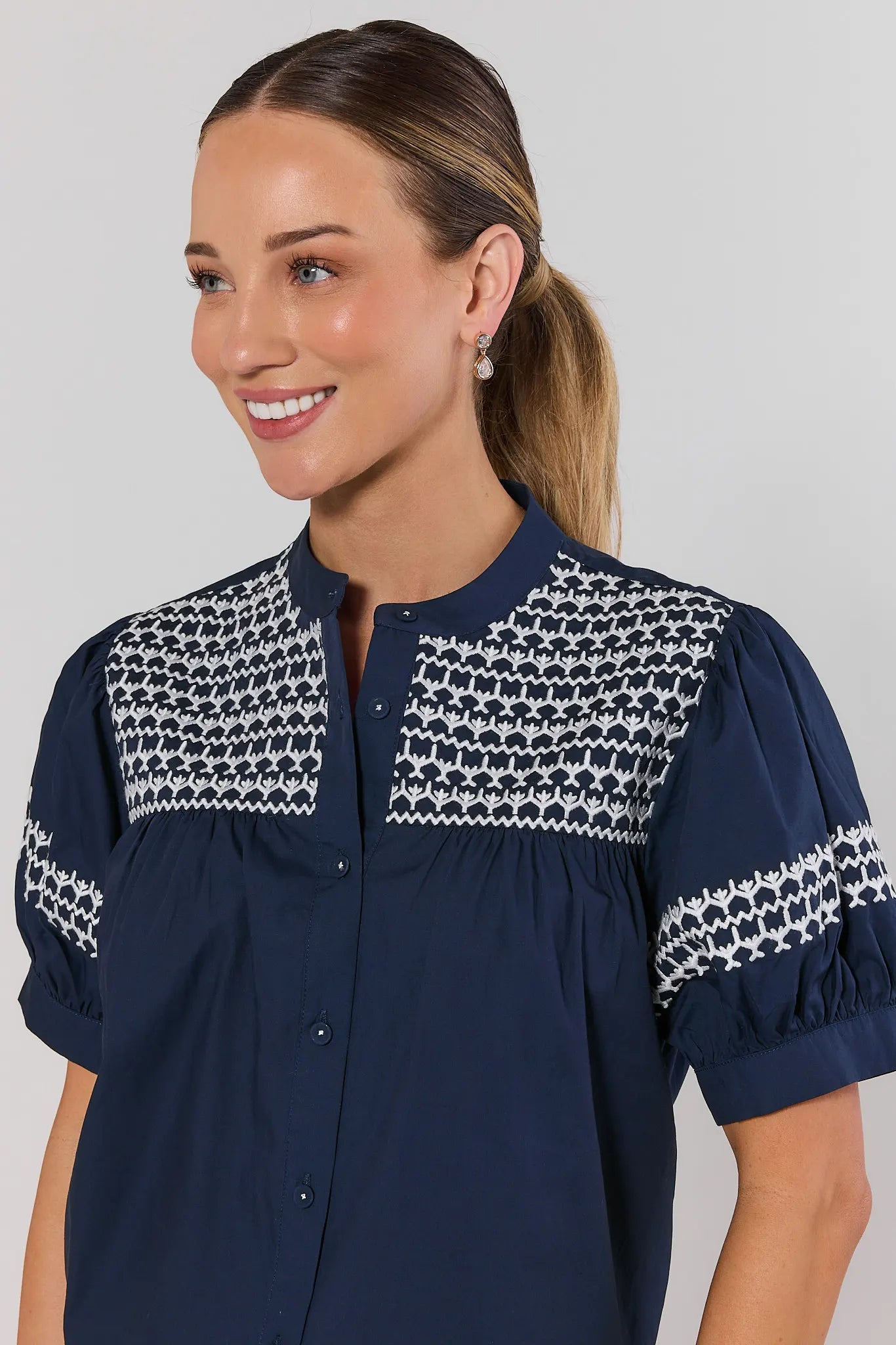 close up Woman wearing a navy blue blouse with white patterned accents on a plain background