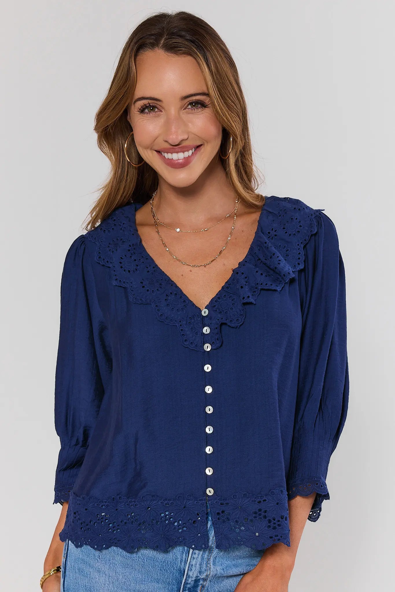 Woman wearing a blue blouse with lace details on a plain background