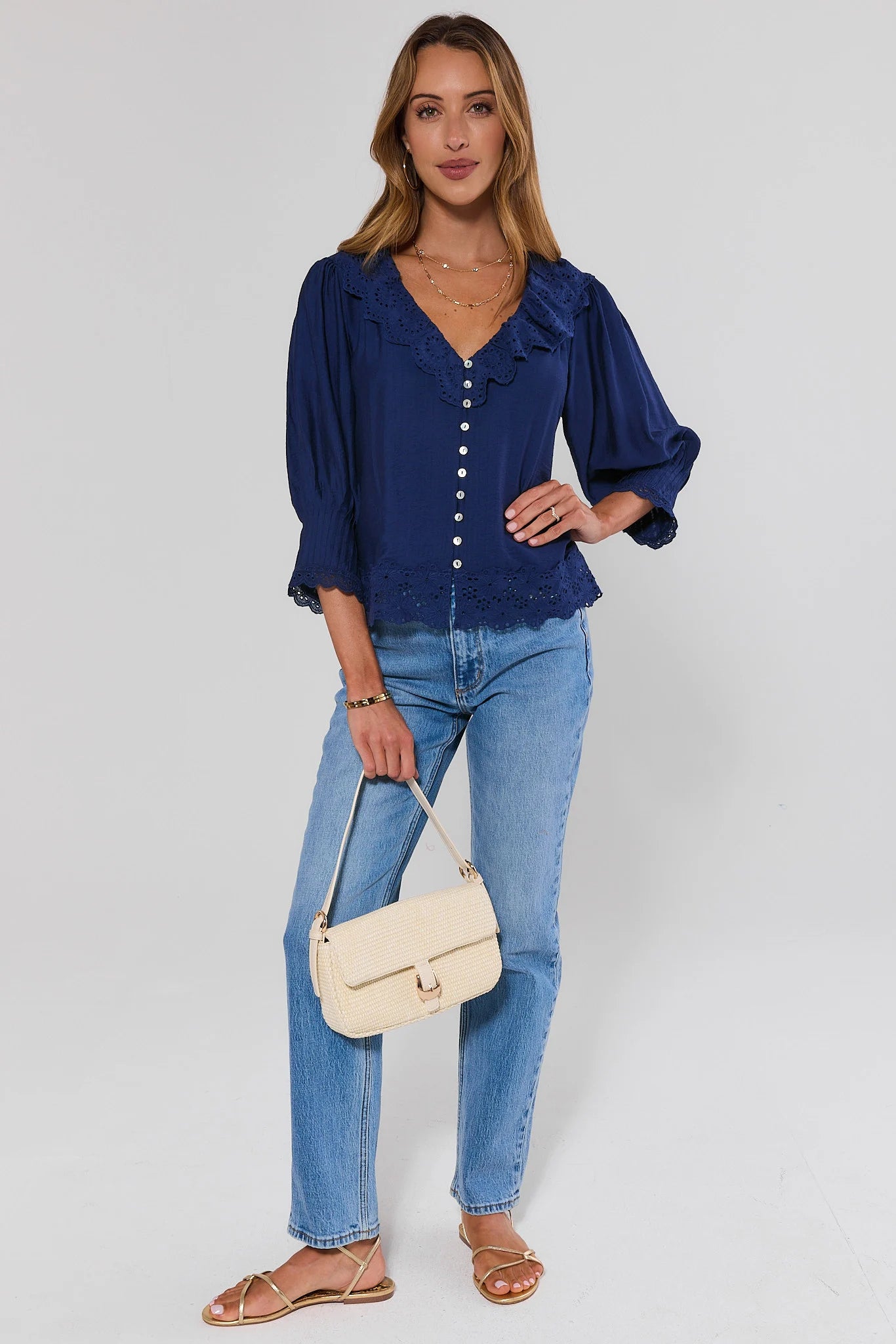Woman wearing a blue blouse, jeans, and carrying a beige handbag on a plain background