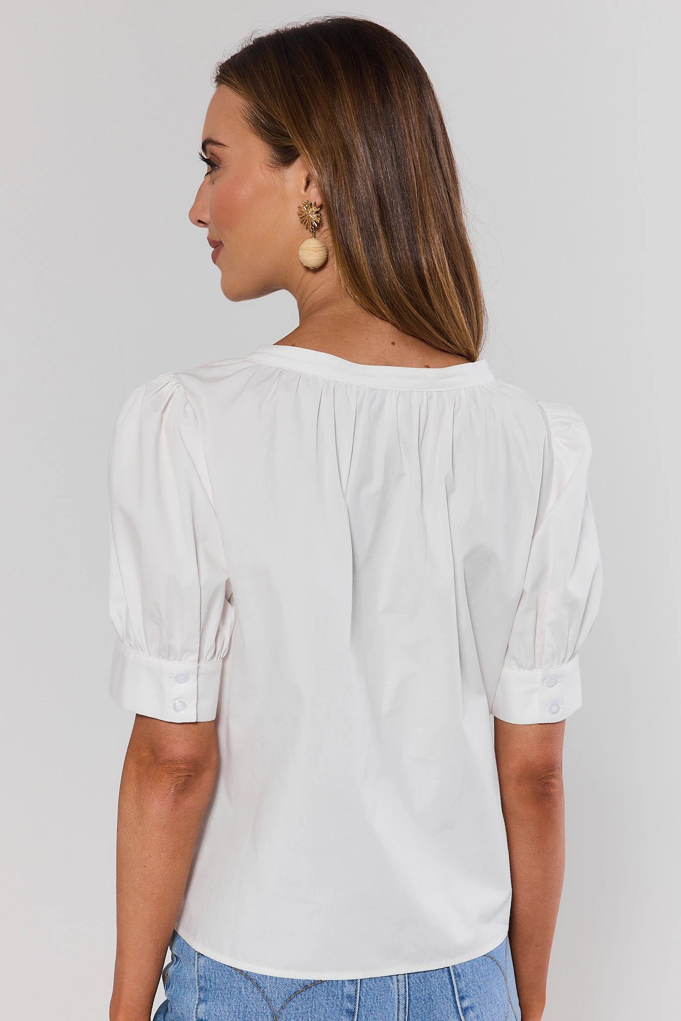 Woman wearing a white blouse with short sleeves against a plain standing background