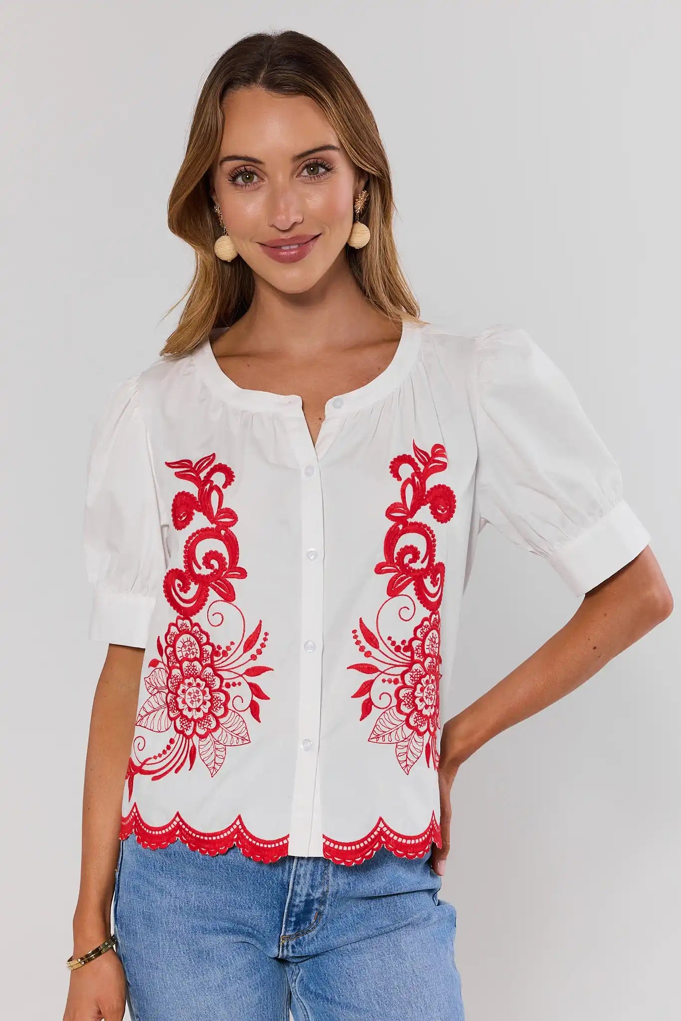Woman wearing a white blouse top with red floral embroidery on a plain background