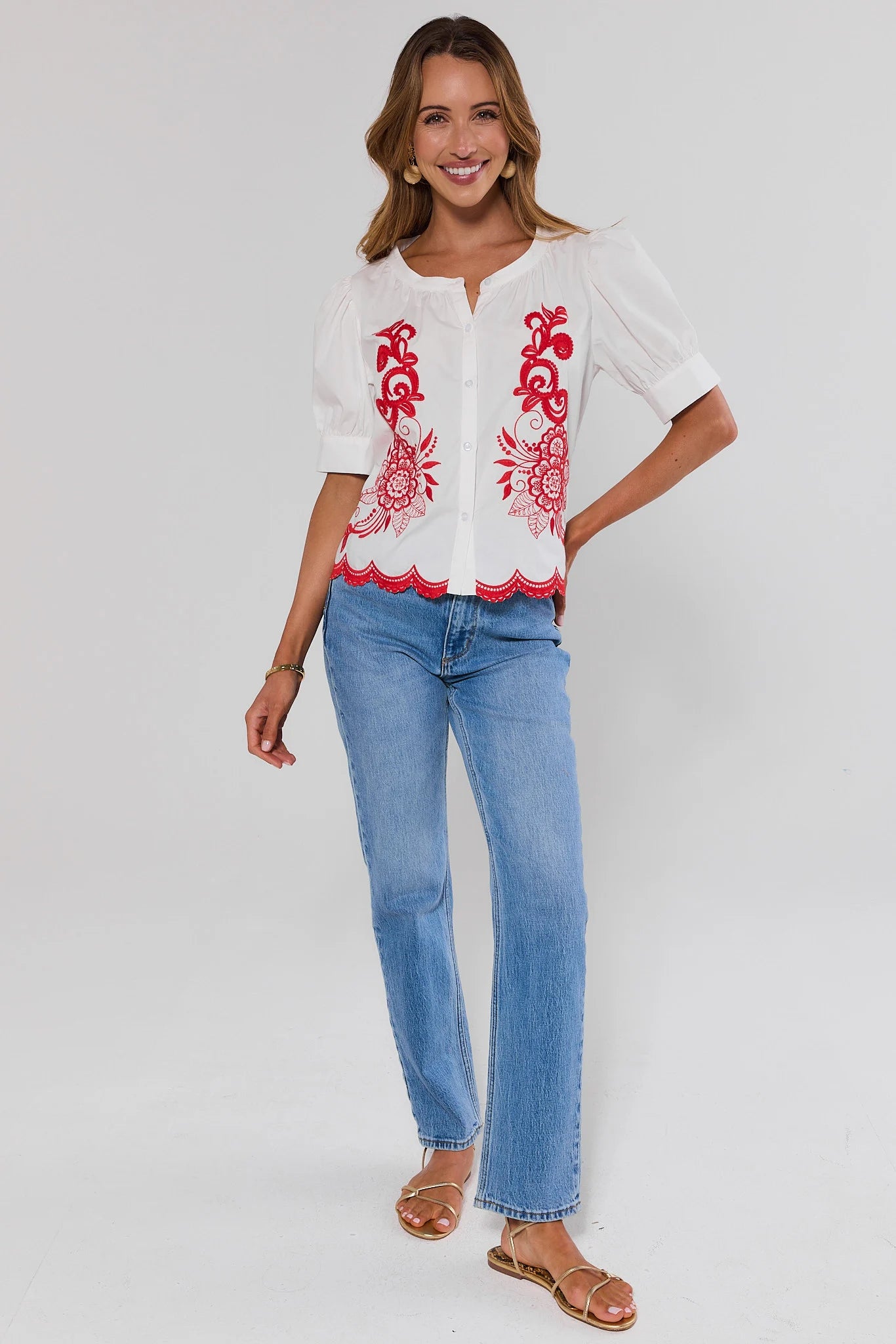 Woman wearing a white blouse with red embroidery and blue jeans on a white background standing