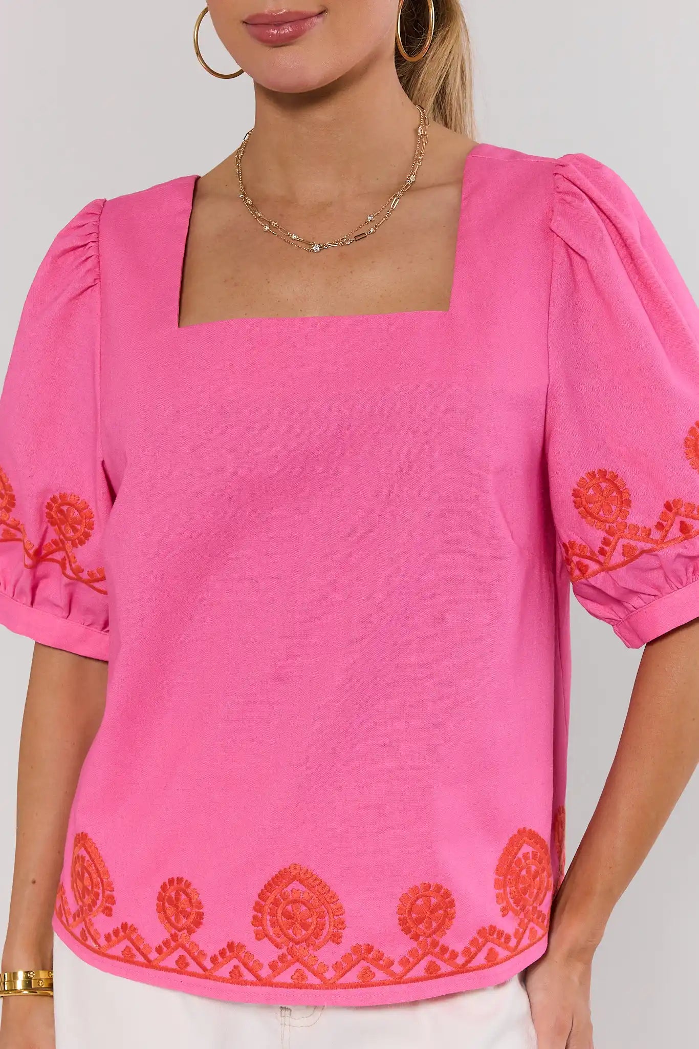 close up Woman wearing a pink blouse with orange embroidery on a plain background