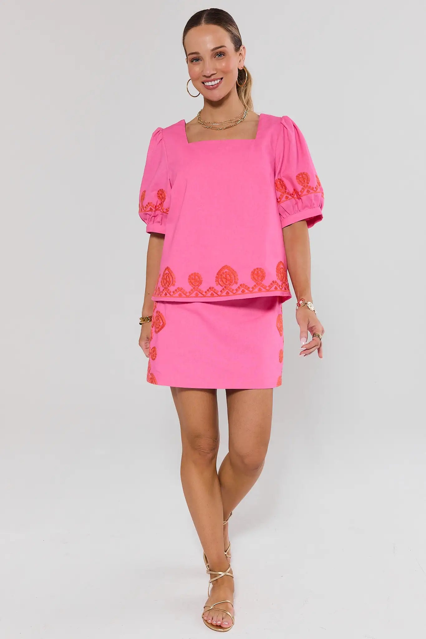 Woman wearing a pink outfit with orange embroidery on a white background