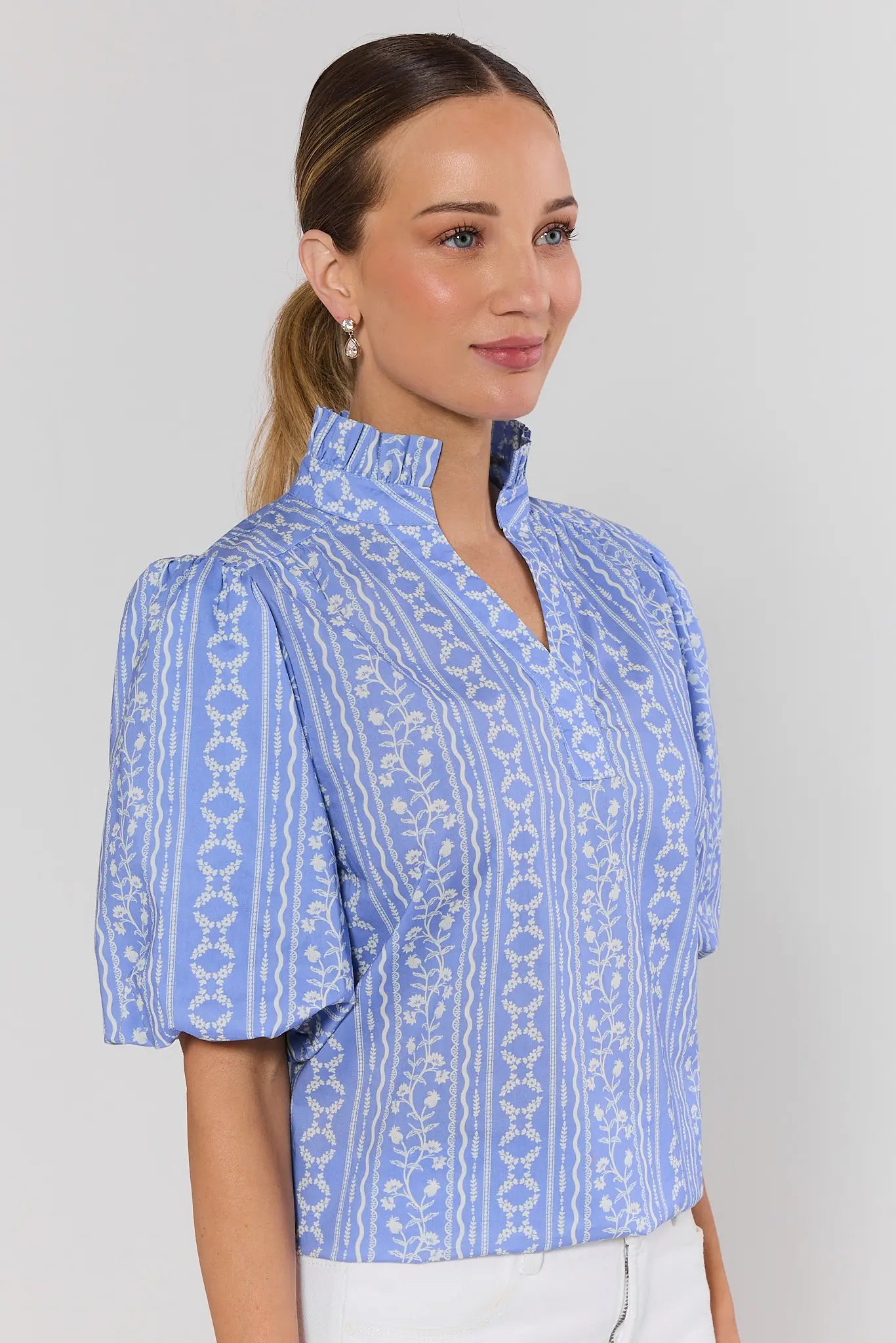 side shot Woman wearing a blue patterned blouse against a plain background