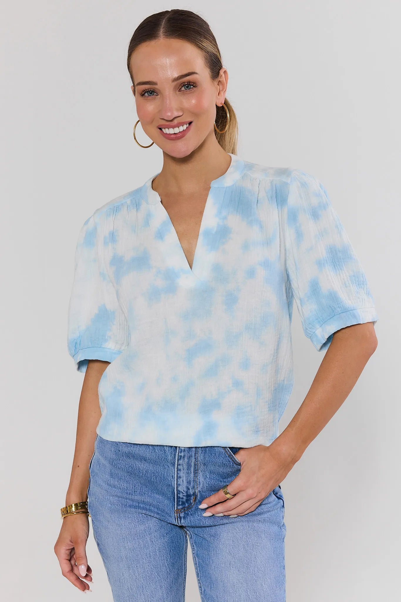 Woman wearing a blue tie-dye blouse and jeans on a plain background