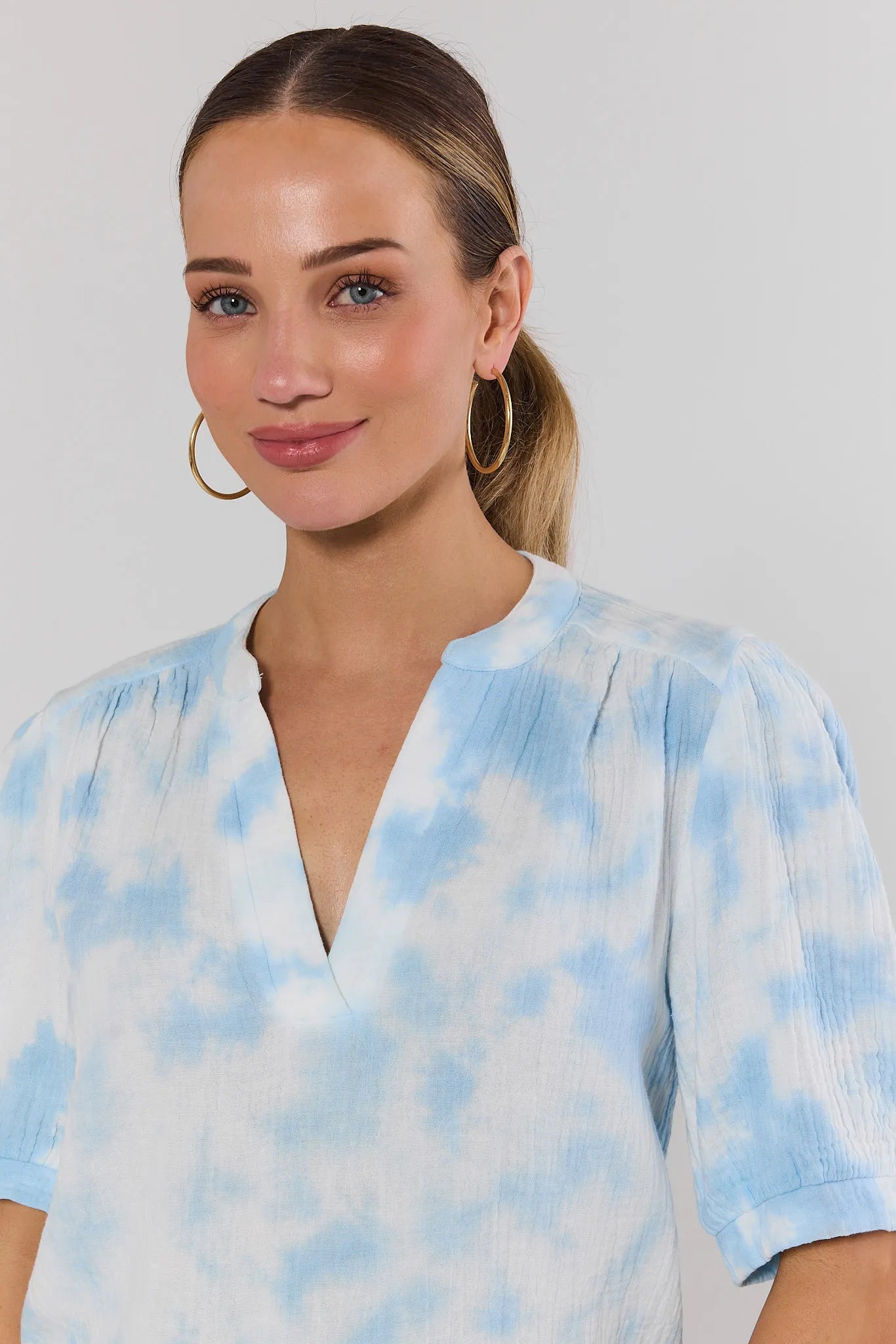 close up Woman wearing a blue and white tie-dye shirt against a plain background