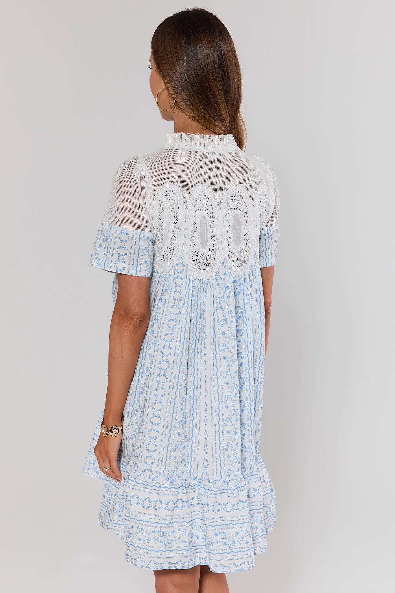 Woman standing wearing a light blue dress with lace details on a plain background