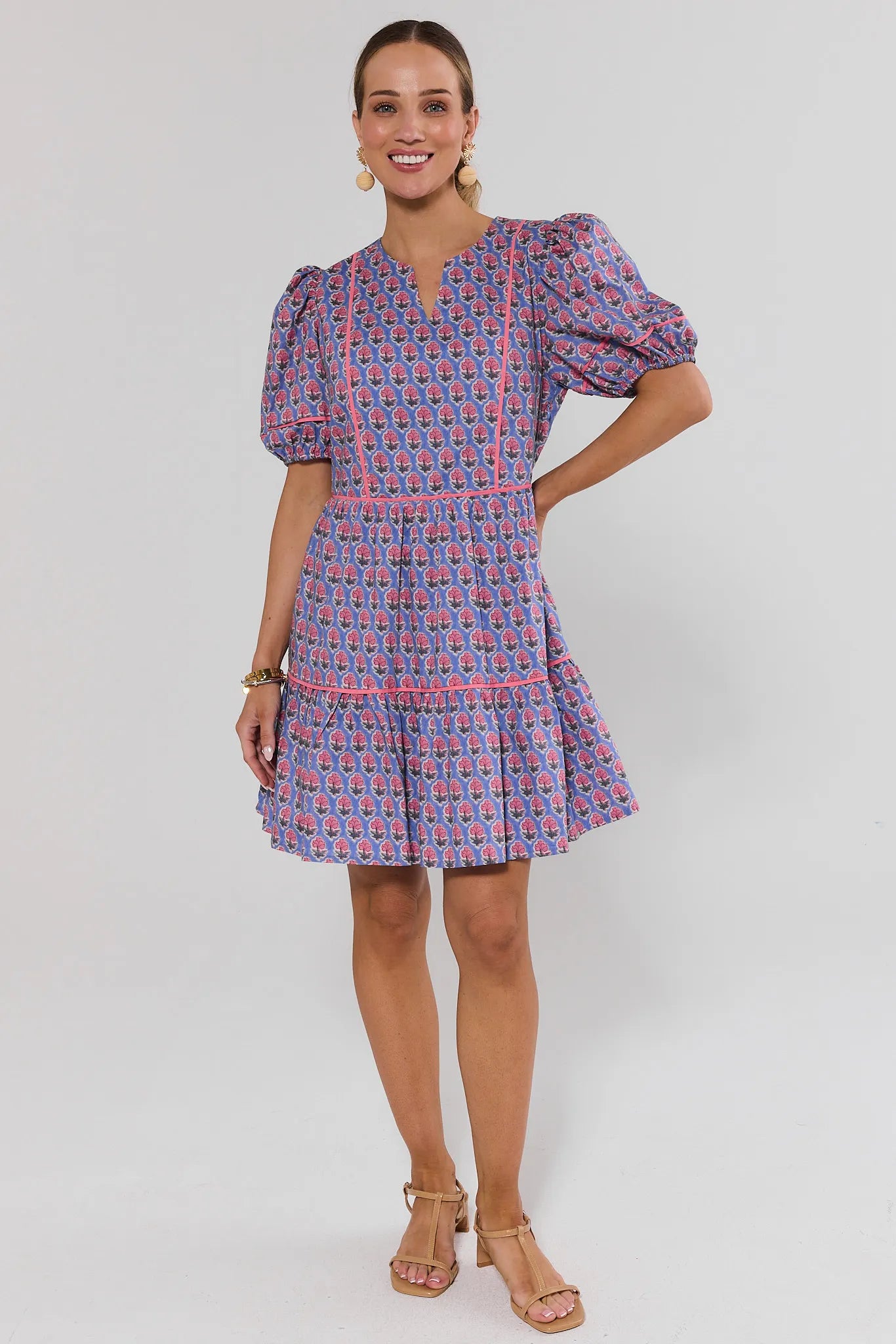 Woman standing wearing a patterned dress on a plain background