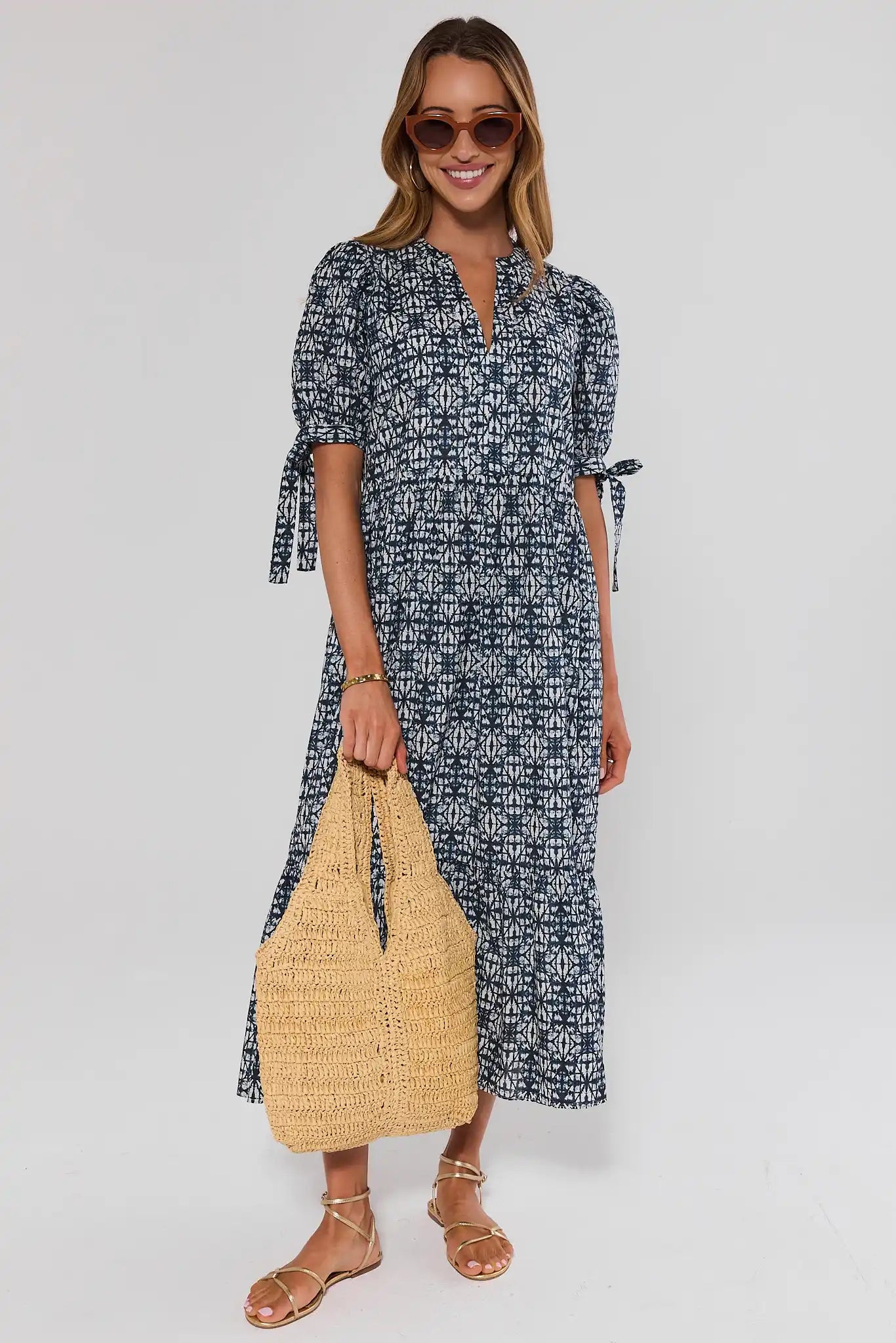 Woman wearing a black and white patterned dress holding a straw bag on a white background
