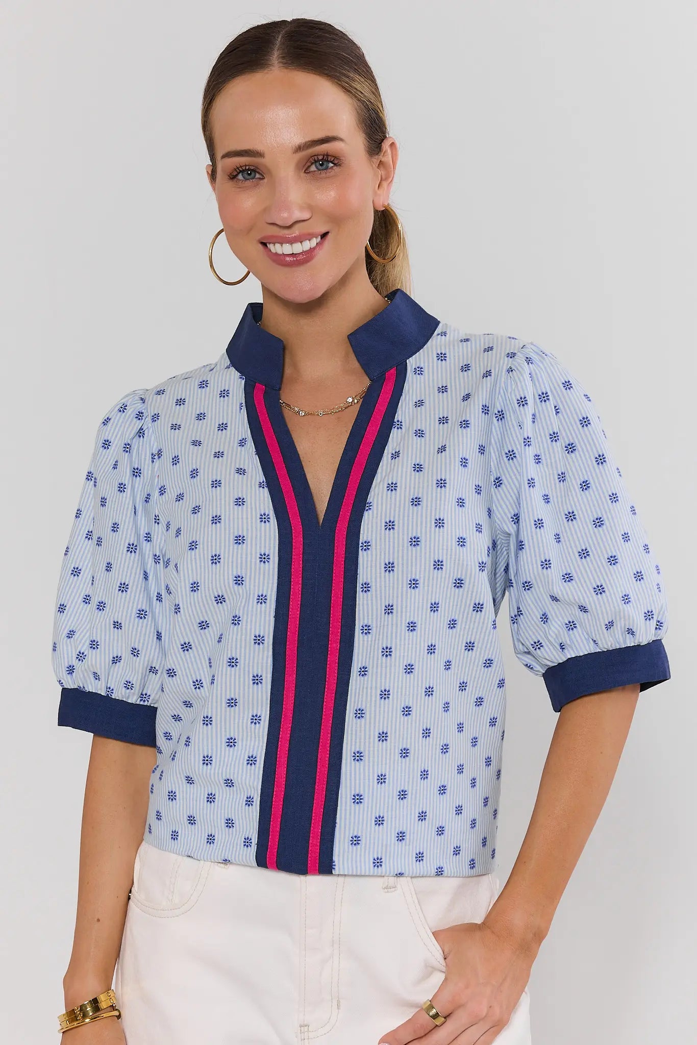 Woman wearing a patterned blouse with blue and pink accents on a plain background