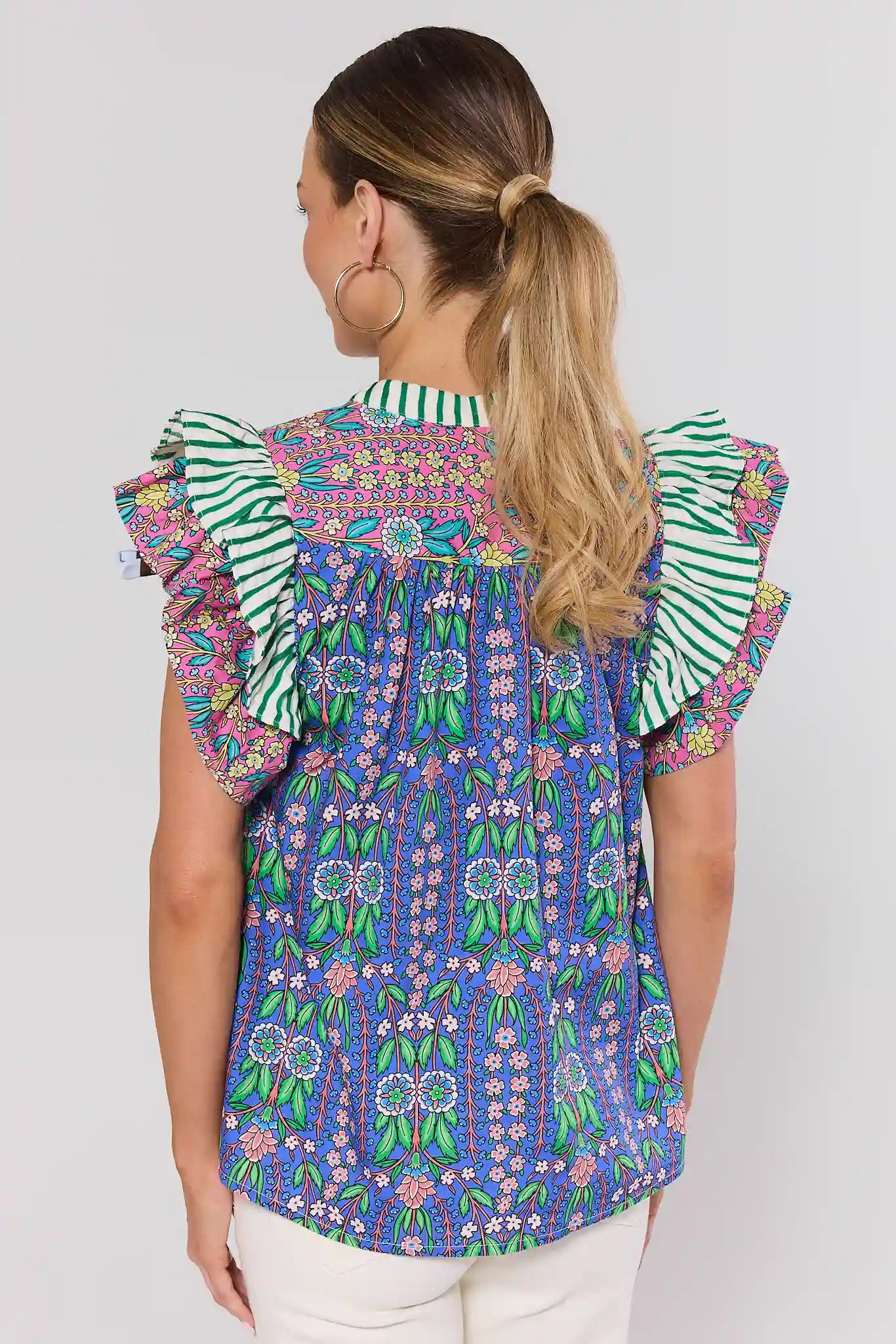 Woman standing wearing a colorful patterned blouse with ruffled sleeves on a white background
