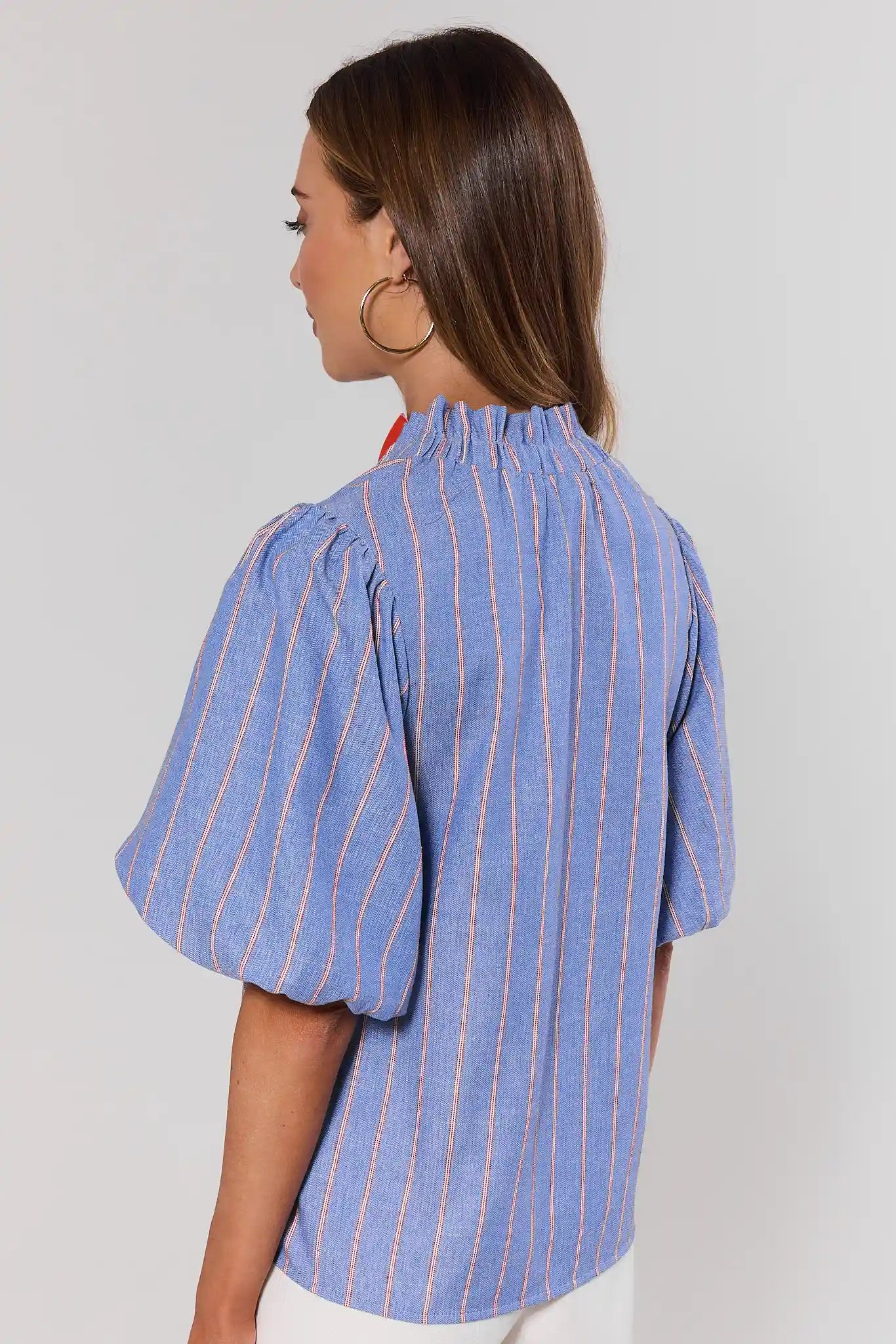 Woman wearing a blue striped shirt with puffed sleeves on a plain background standing