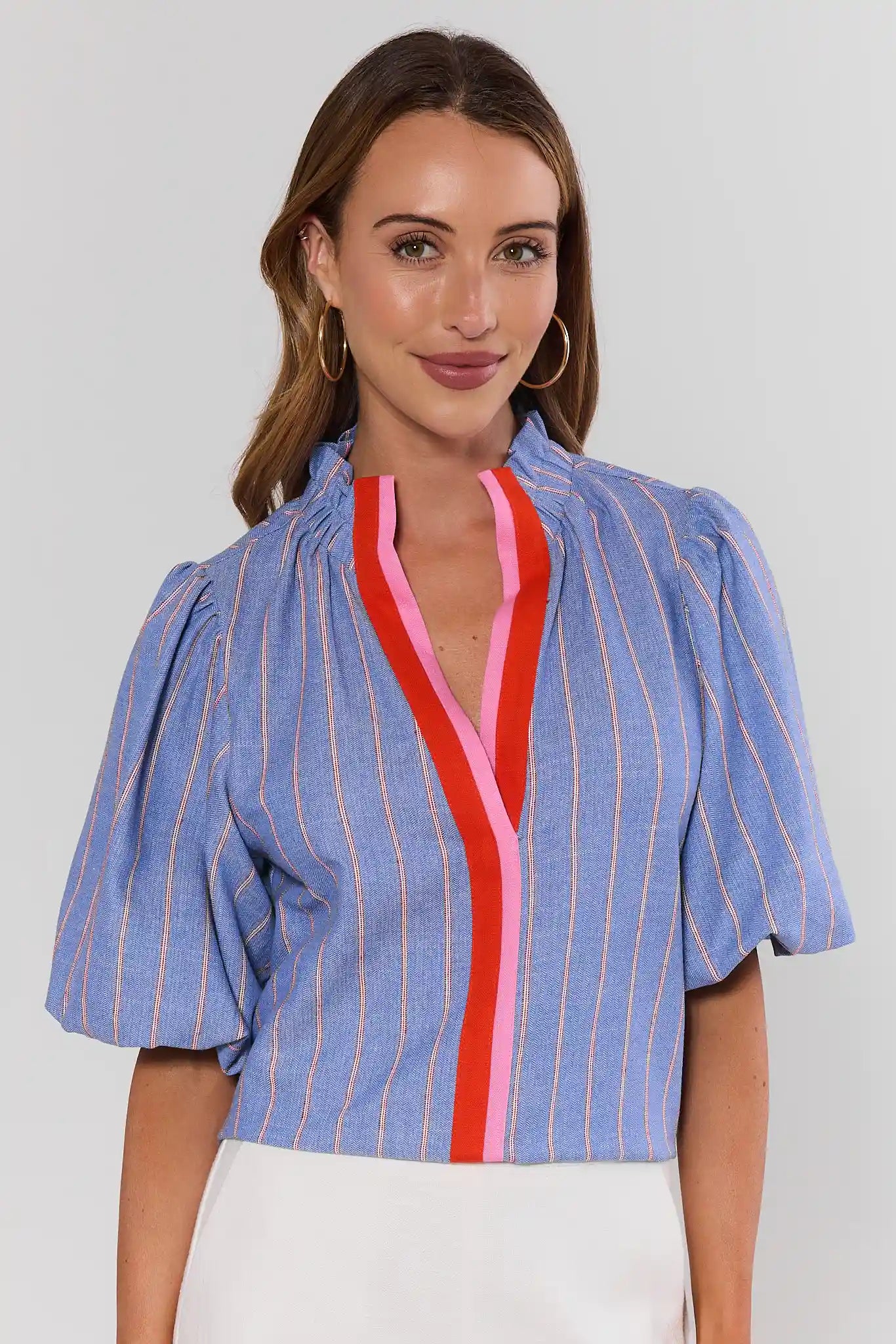 Woman wearing a blue striped blouse with red and pink accents on a plain background