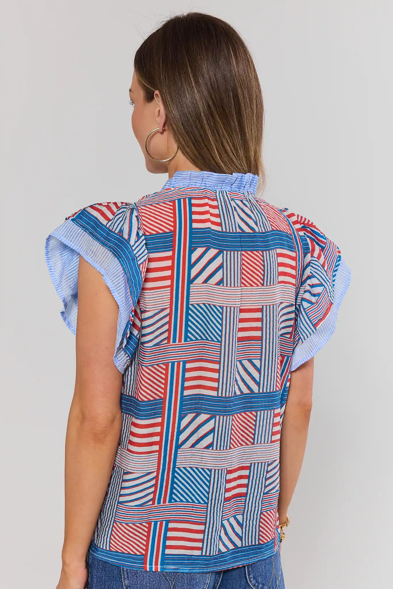 Woman standing wearing a colorful patterned shirt with short sleeves on a plain background
