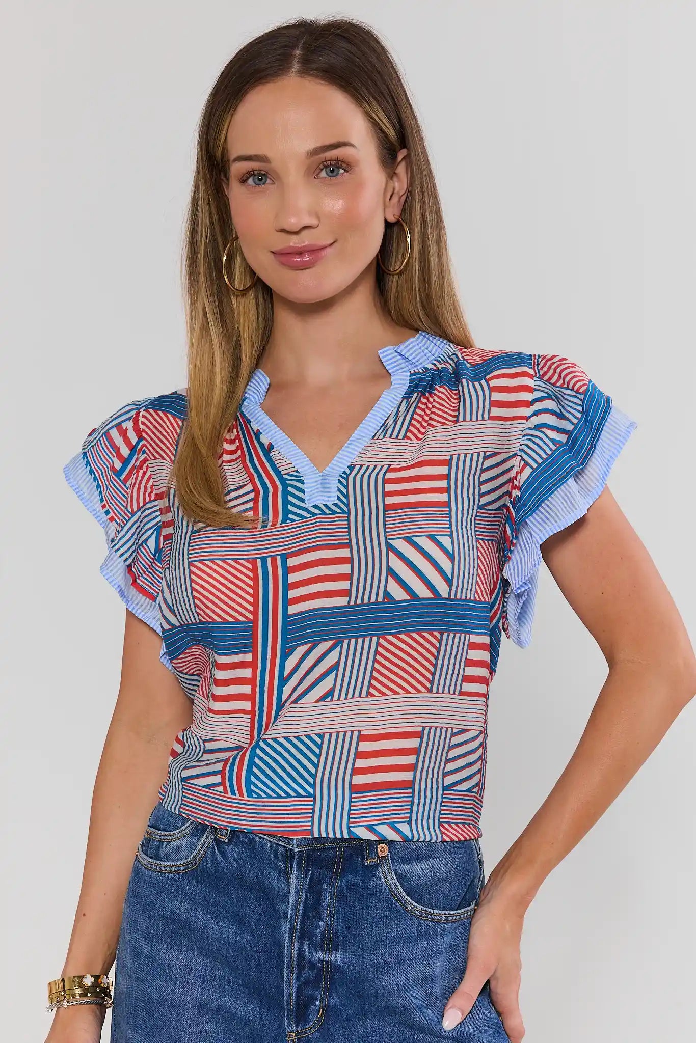 Woman wearing a colorful patterned top with blue jeans on a plain background