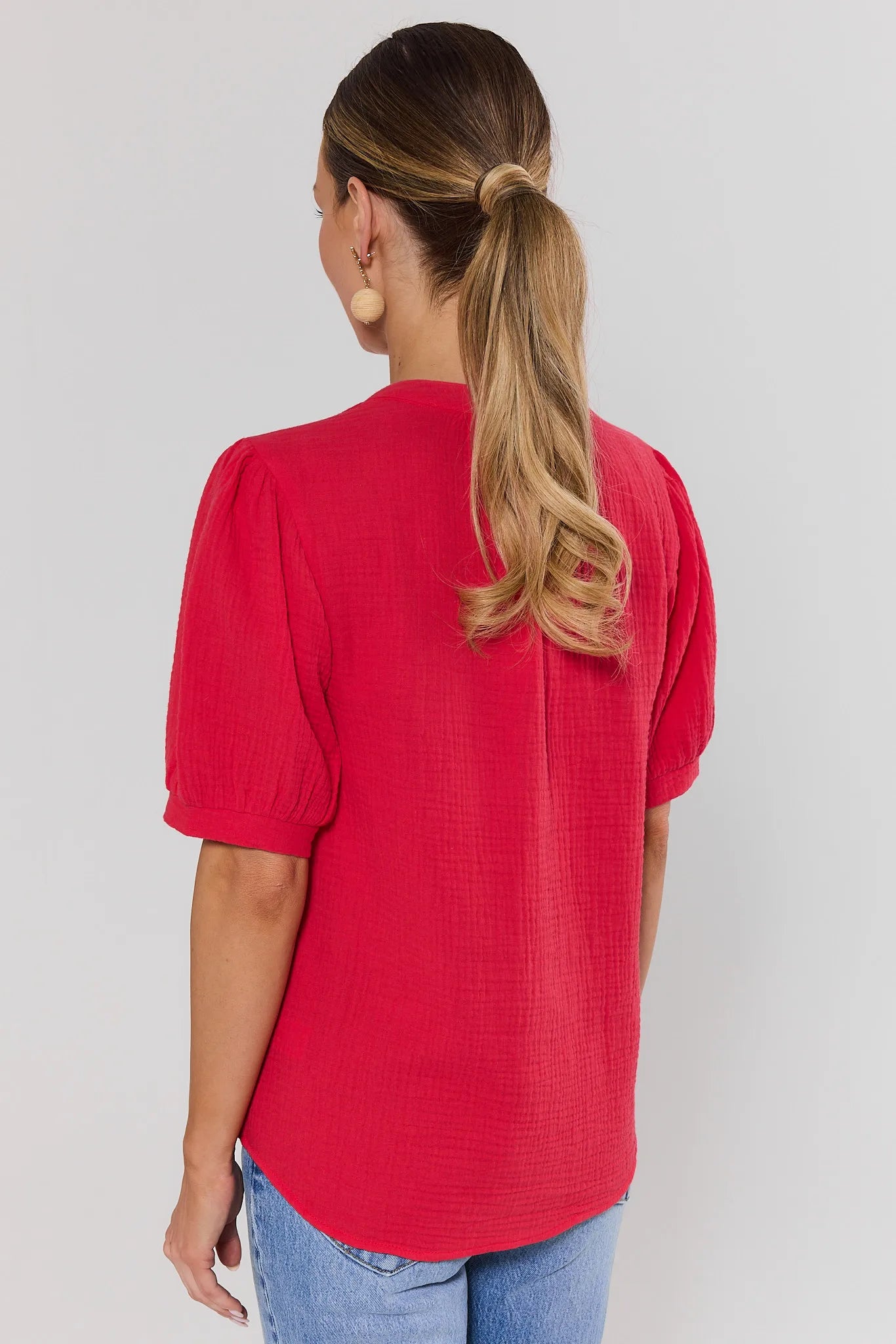 Woman standing wearing a red blouse with puff sleeves on a plain background