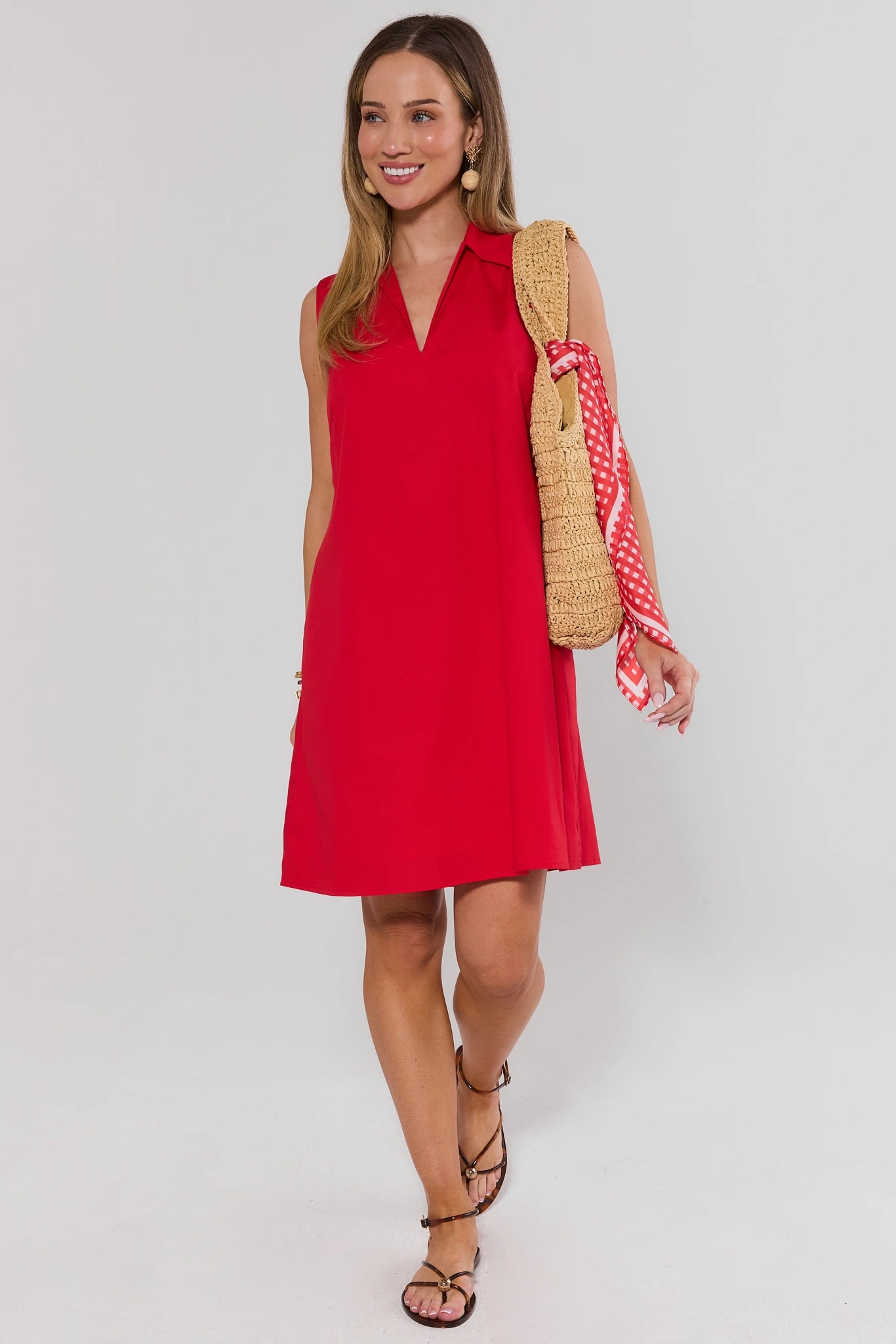 Woman wearing a red dress with a straw bag on a white background