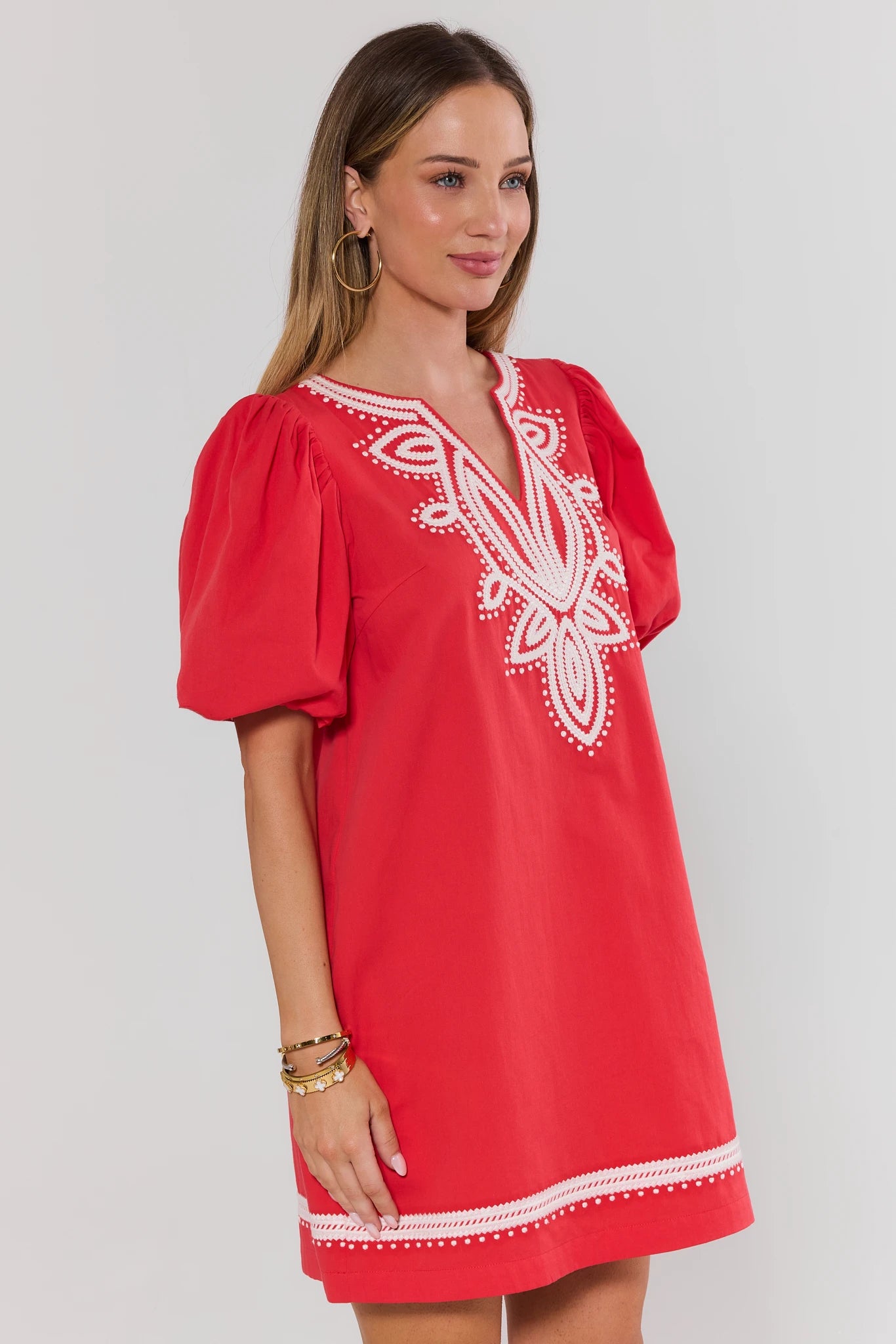Woman wearing a red dress with white embroidery on a plain background side