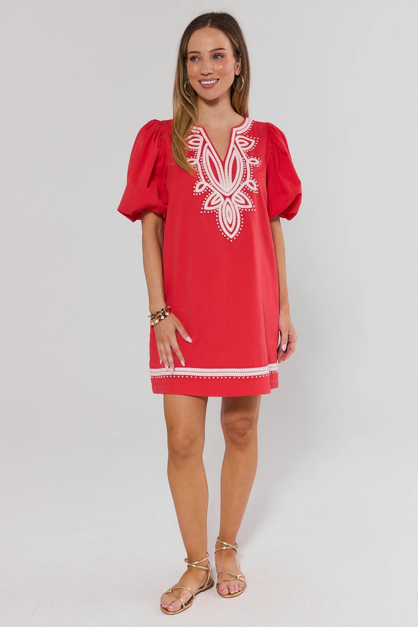 Woman wearing a roxanne red dress with white embroidery on a plain background