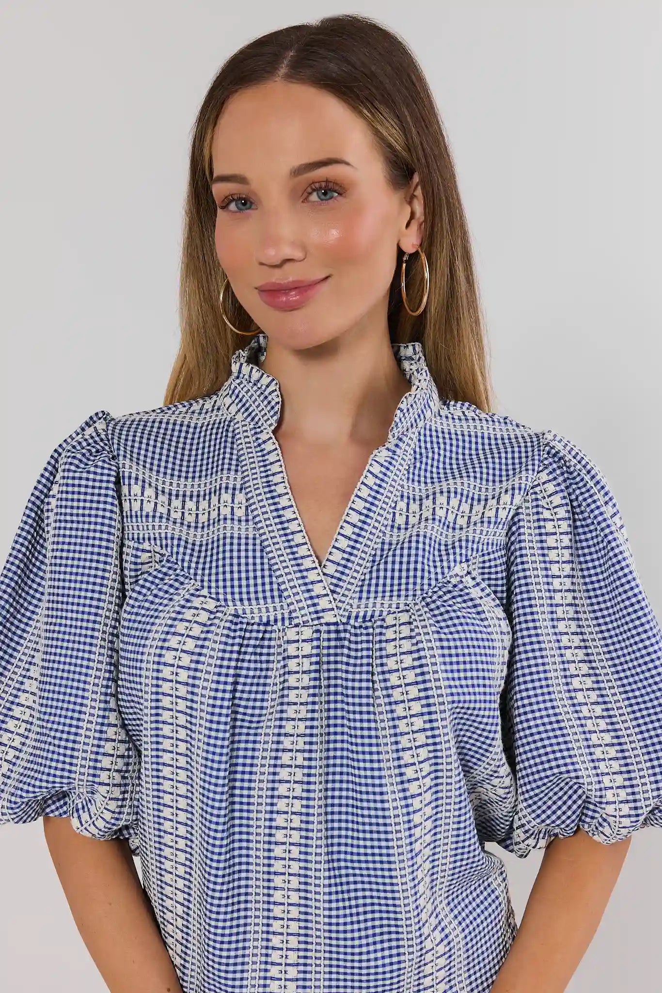 Woman wearing a blue and white checkered blouse against a gray background close up
