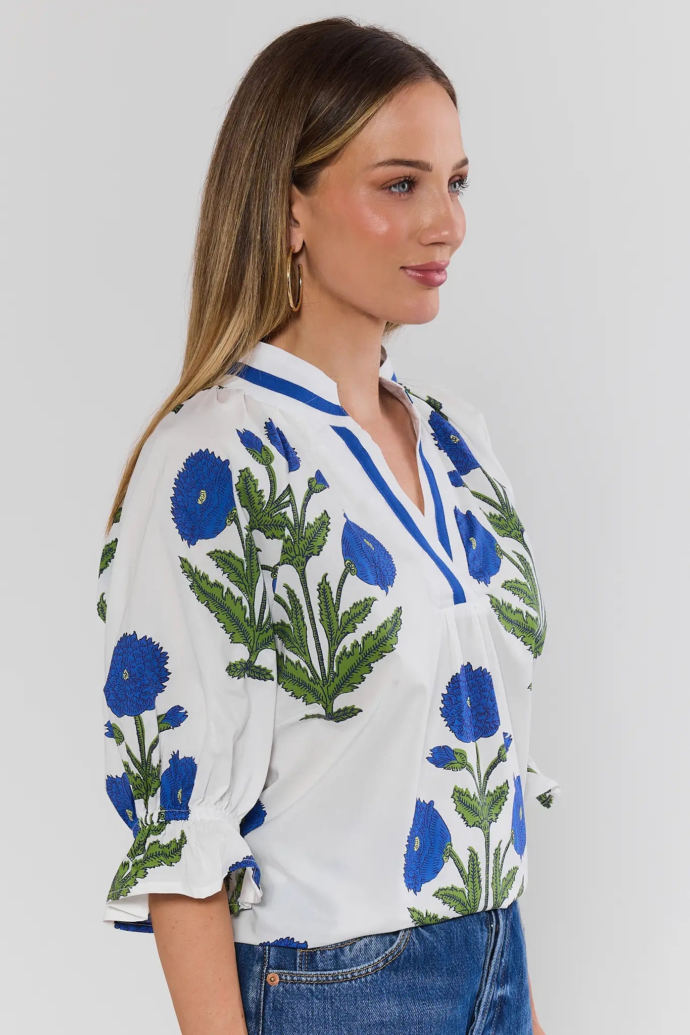 Woman wearing a white blouse with blue floral embroidery on a plain background side