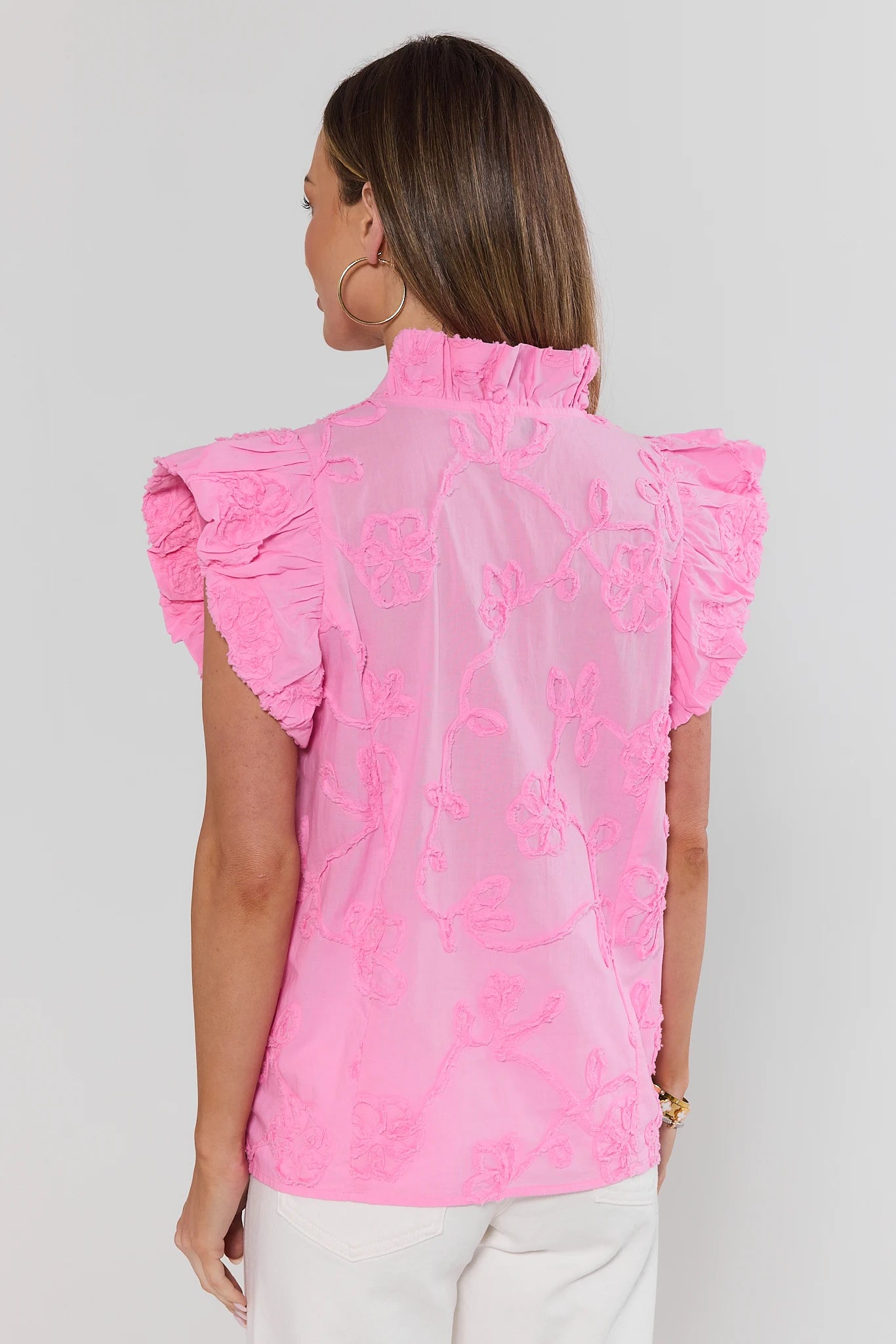 Woman standing wearing a pink embroidered blouse with ruffled sleeves on a plain background