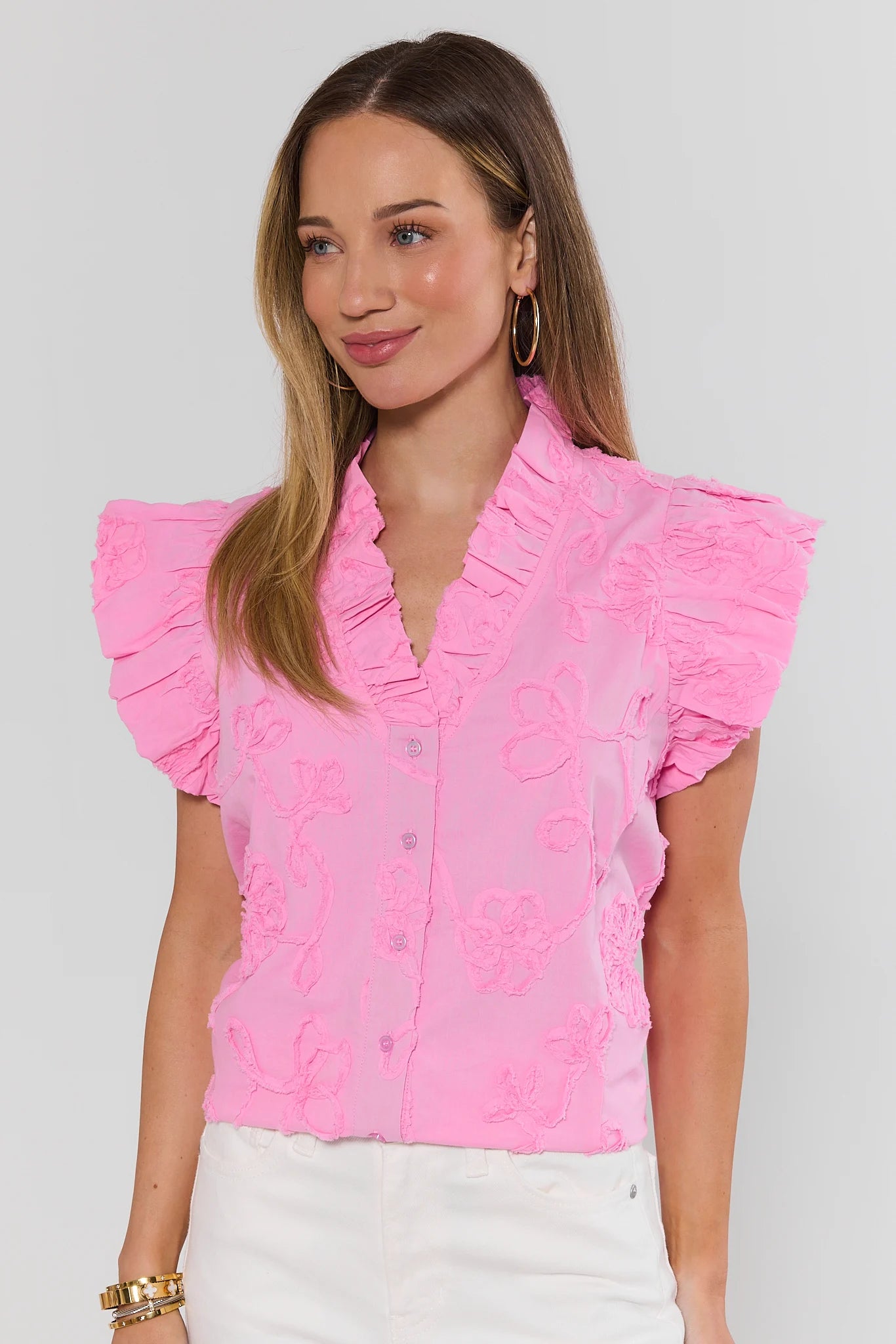 Woman wearing a pink blouse with ruffled sleeves against a white background