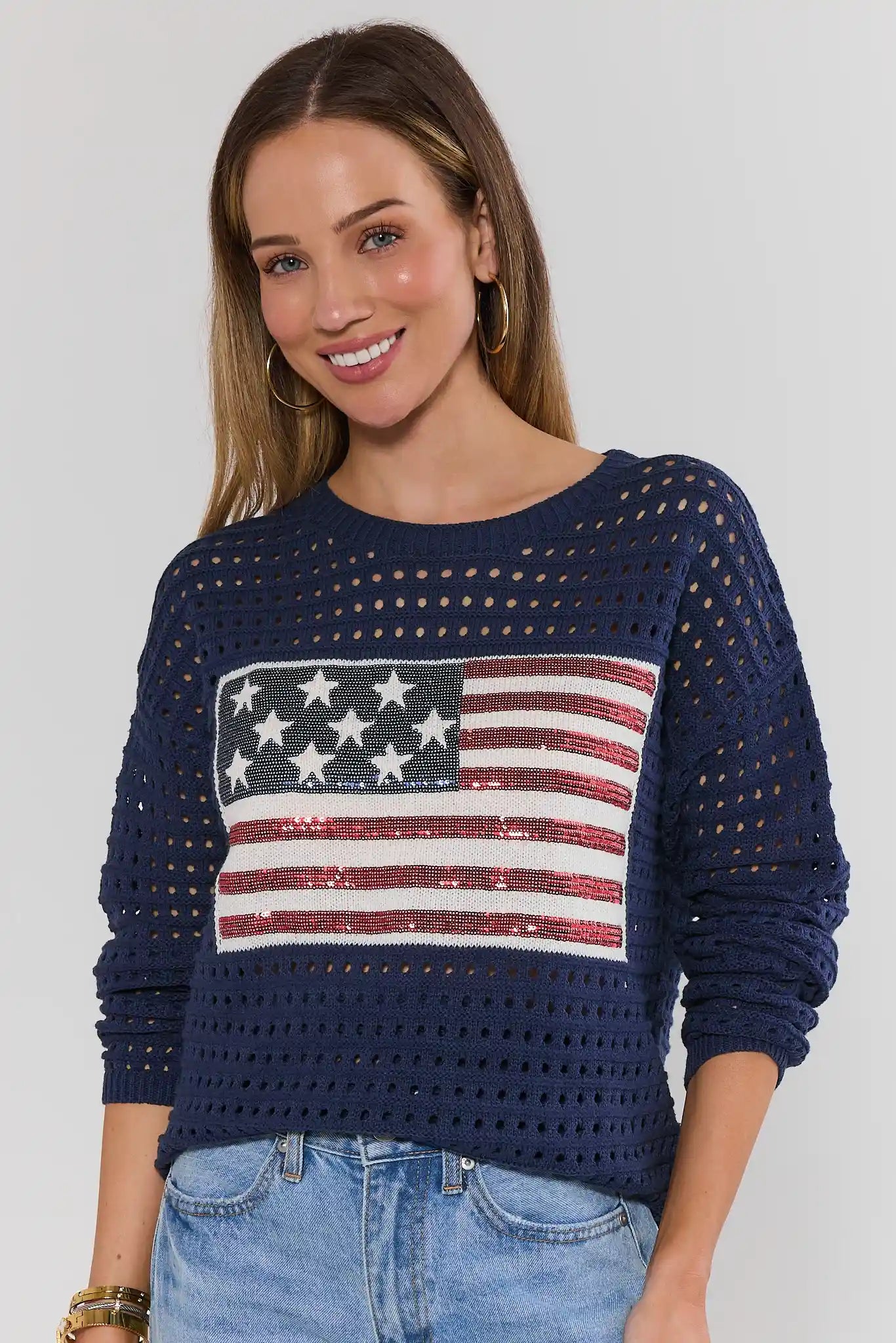 Woman wearing a navy sweater with an American flag design on a plain background