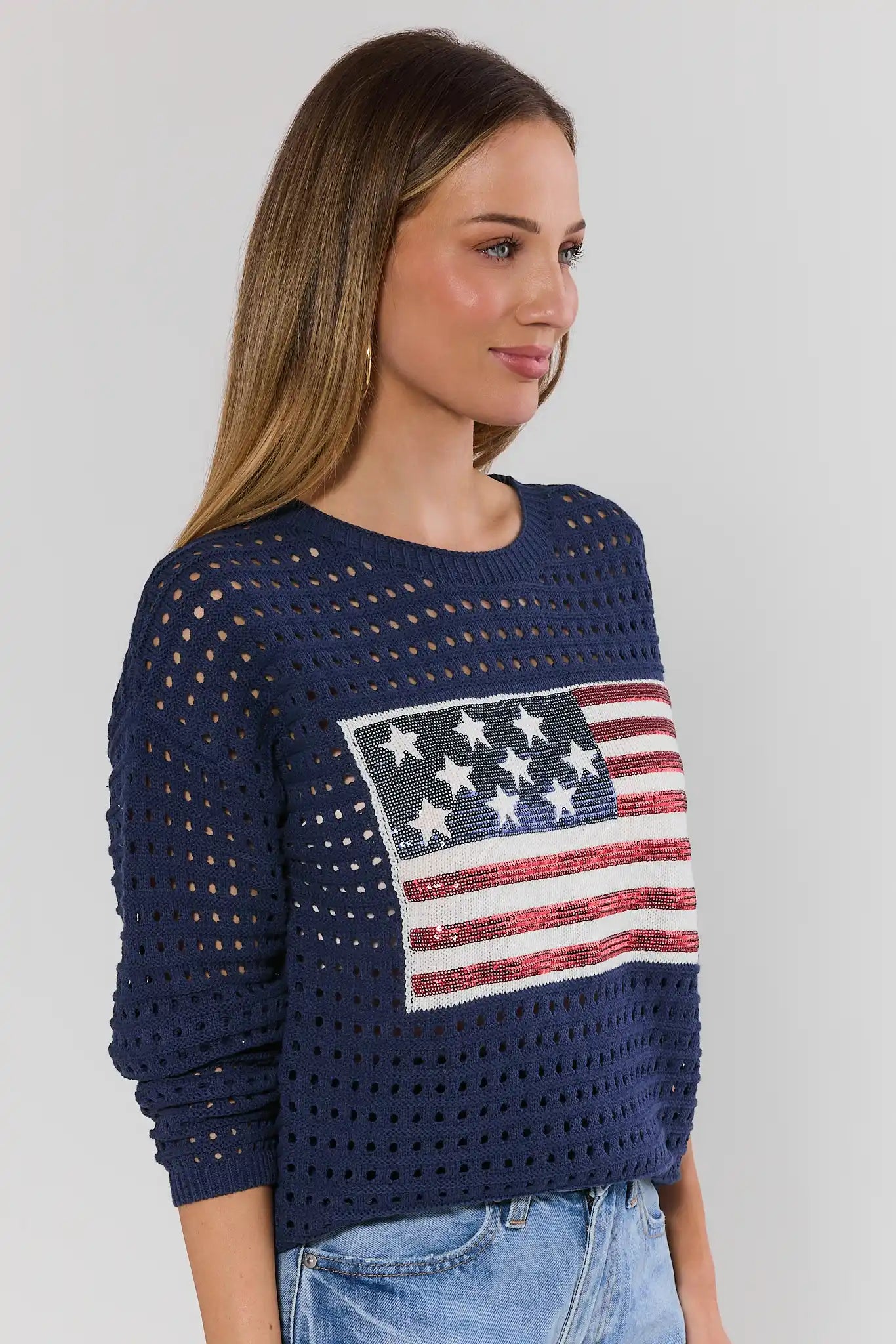 Woman wearing a navy blue sweater with an American flag design on a plain background side