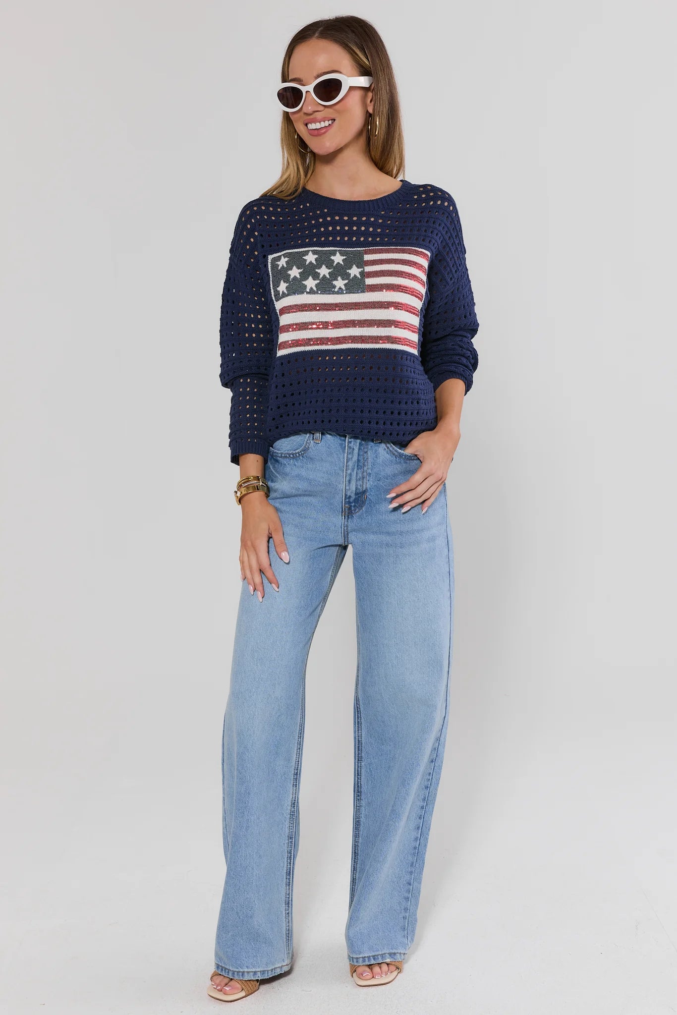 Woman wearing a navy sweater with an American flag design and light blue jeans on a white background