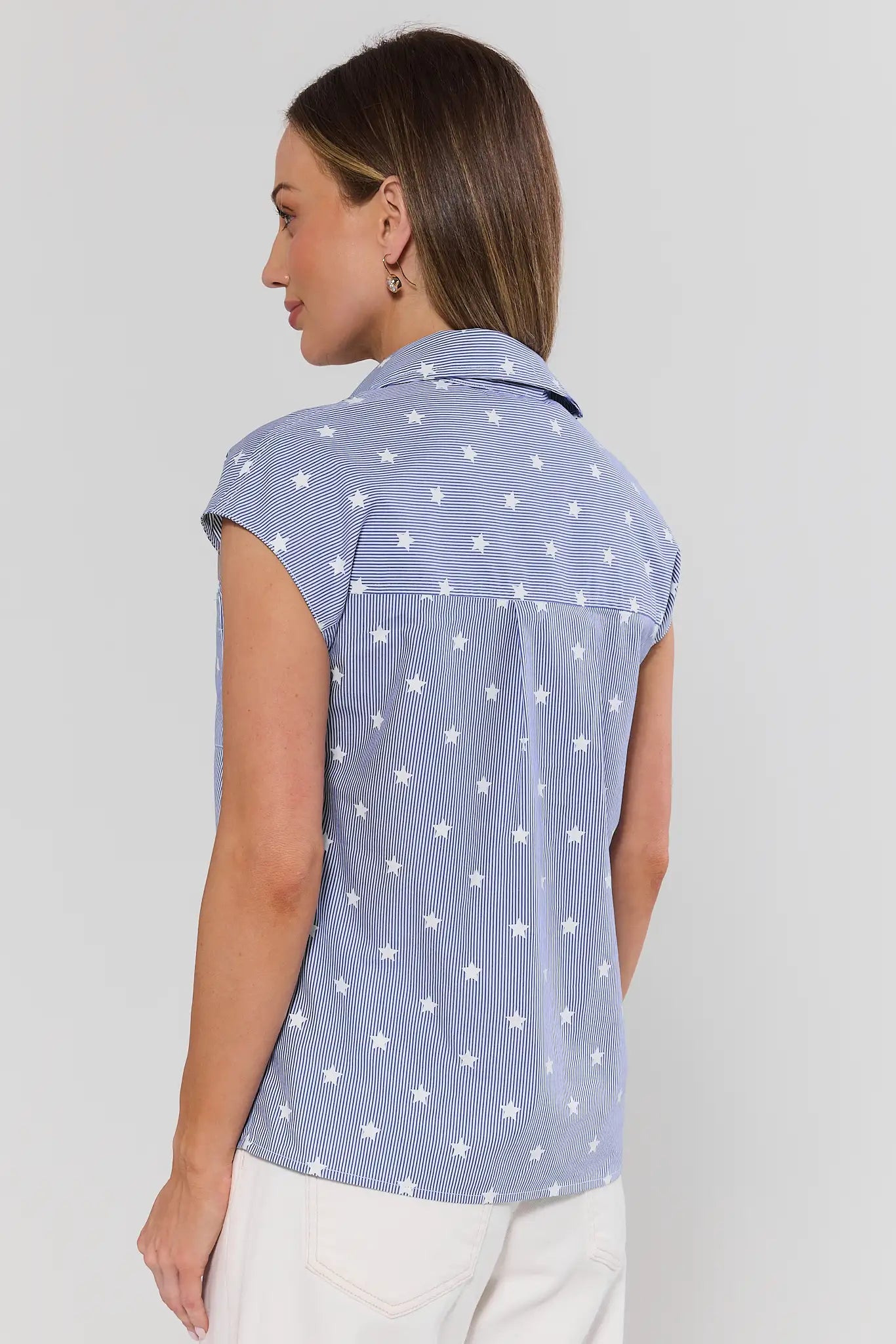 Woman standing wearing a blue sleeveless shirt with white star pattern against a plain background