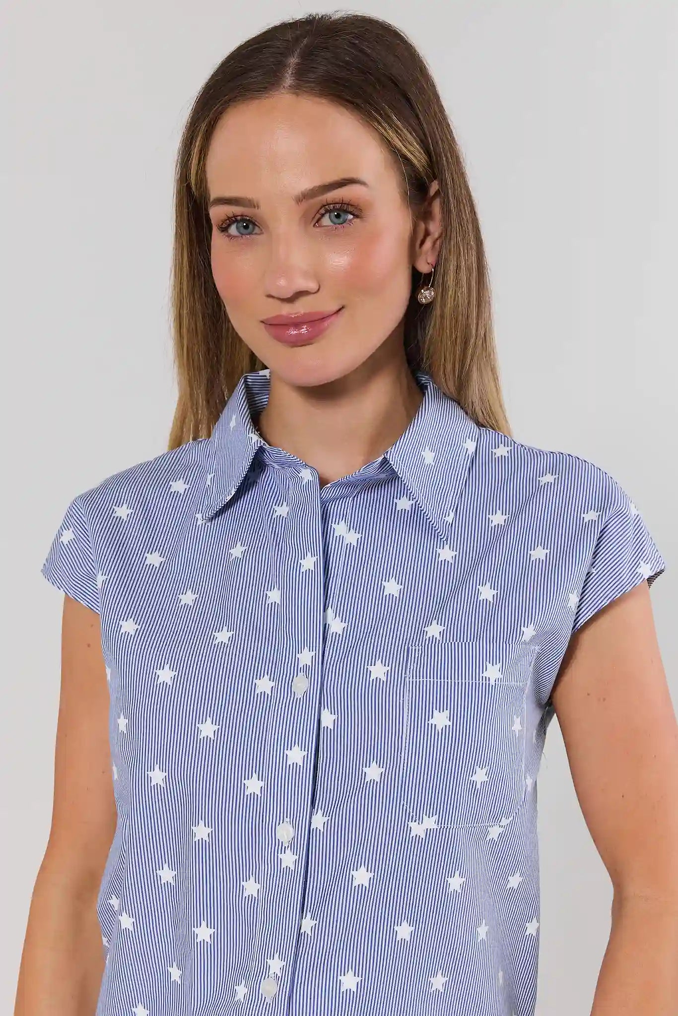 Woman wearing a blue shirt with white star pattern against a plain background close up