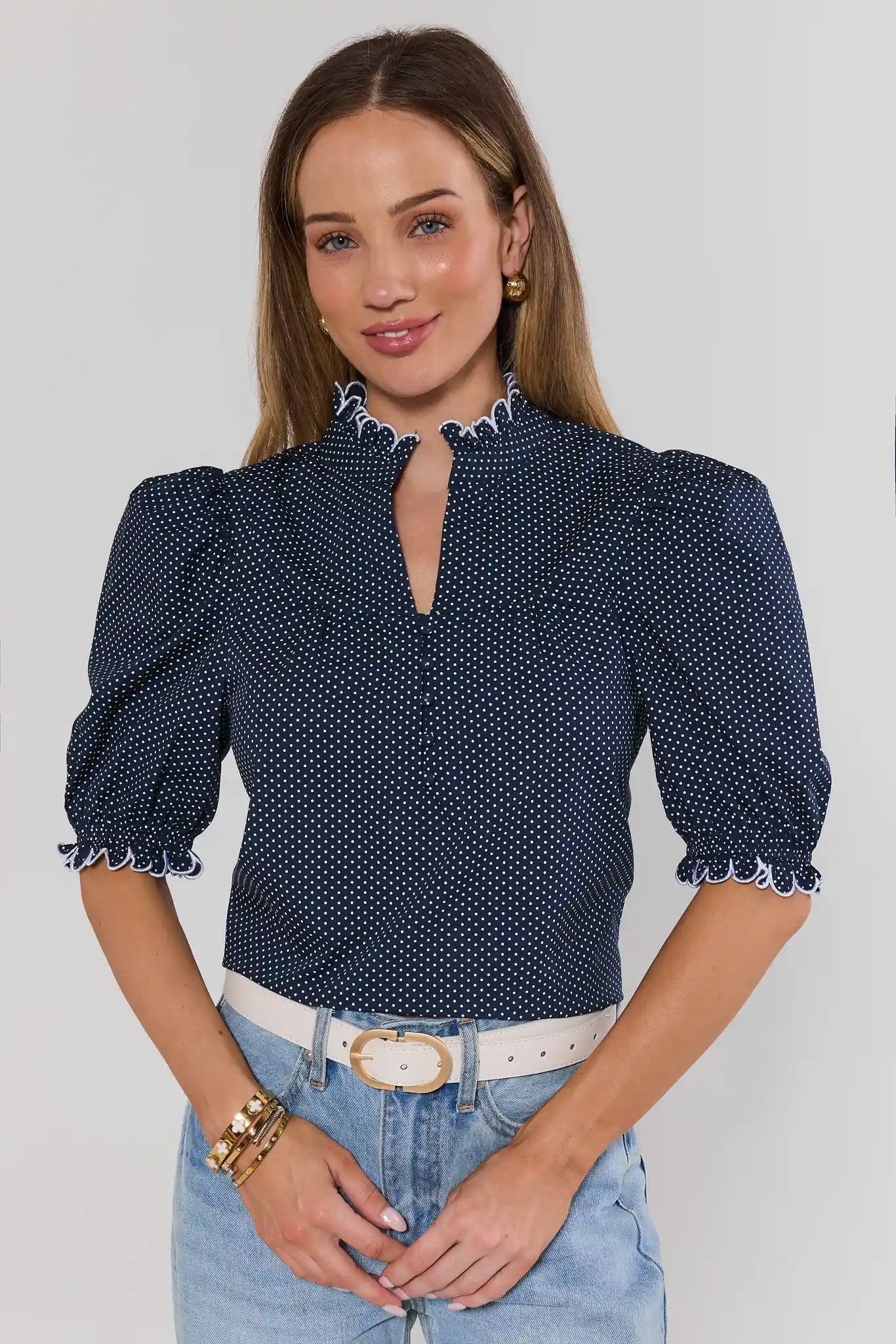 Woman wearing a navy blue polka dot blouse with puffed sleeves against a white background