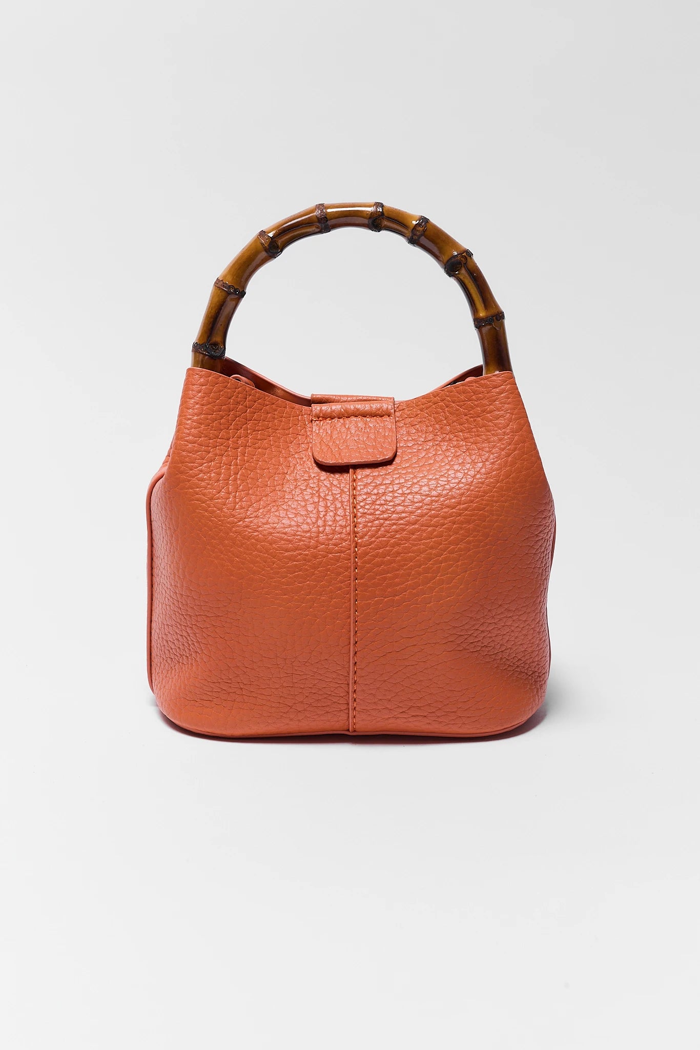 Orange leather handbag with bamboo handle on a light gray background