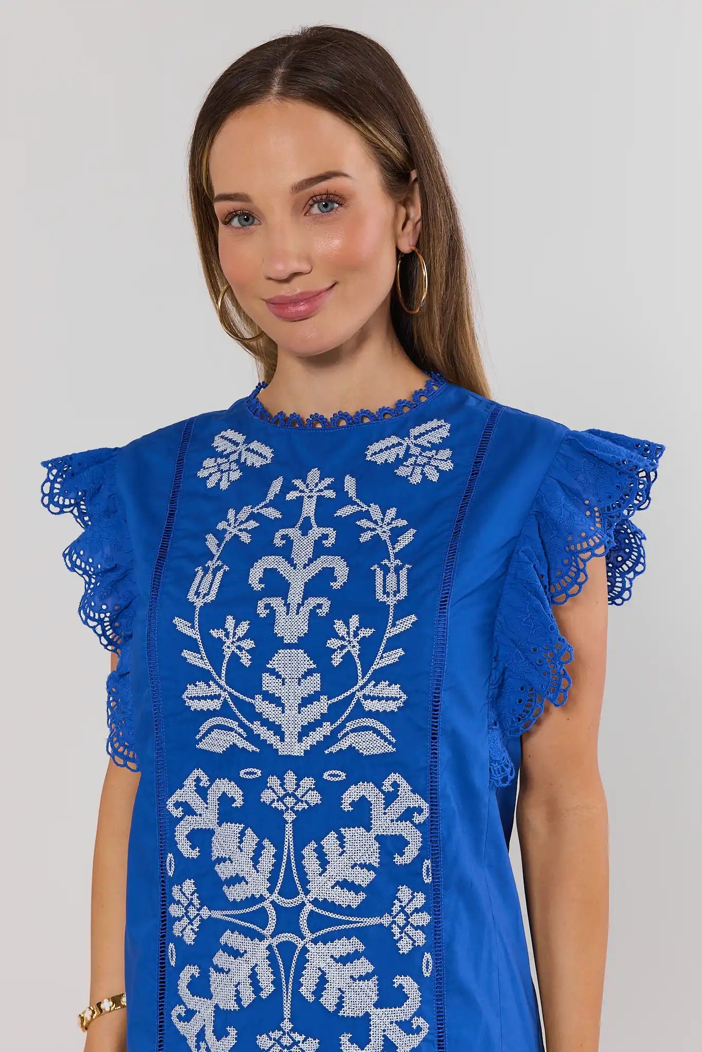 close up Woman wearing a blue dress with white floral embroidery on a plain background